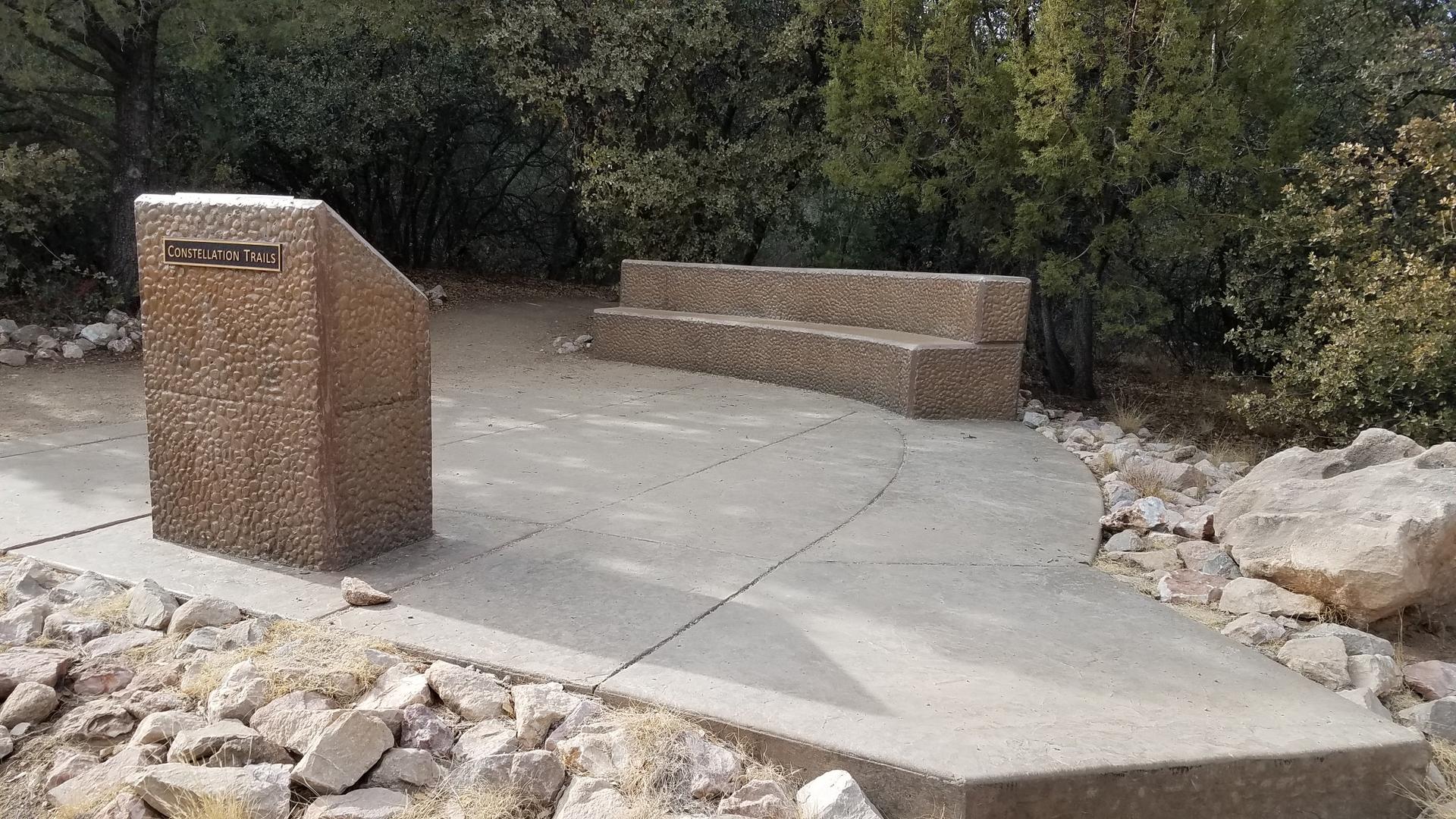 Concrete information kiosk and benches in a wooded area.