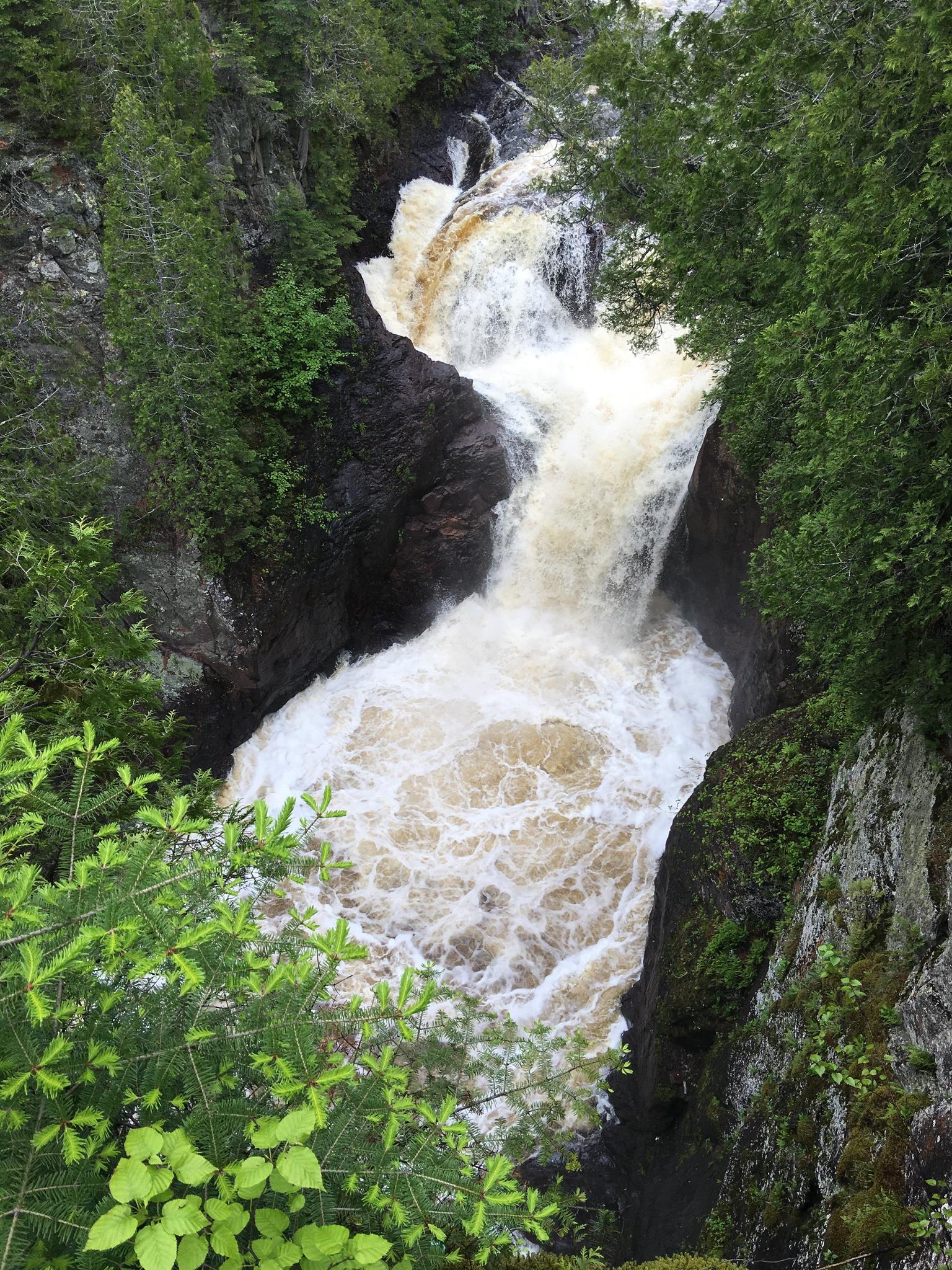 Powerful waterfall cascades into a rocky gorge surrounded by dense green foliage.