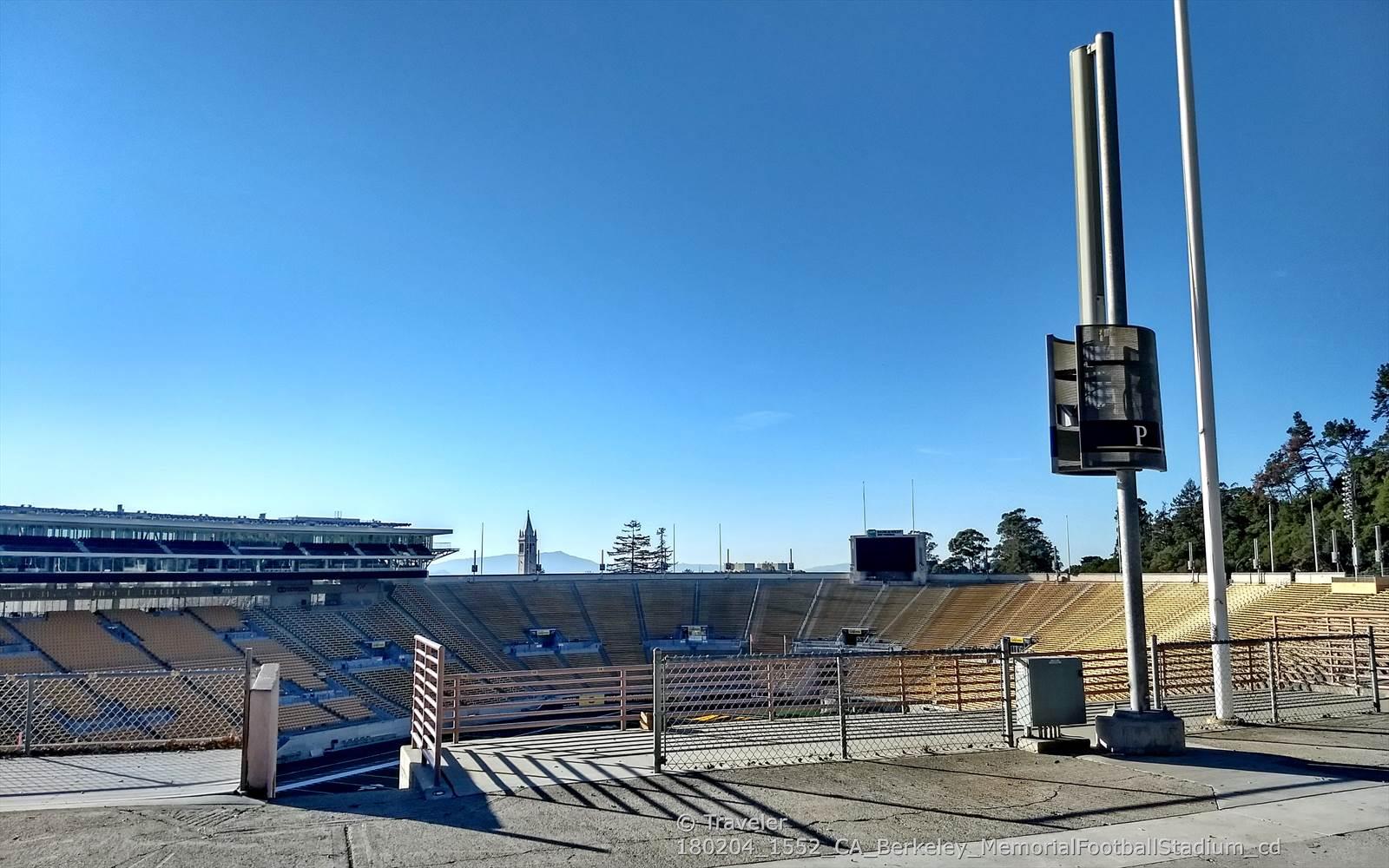 Empty stadium bleachers and a scoreboard under a clear blue sky.