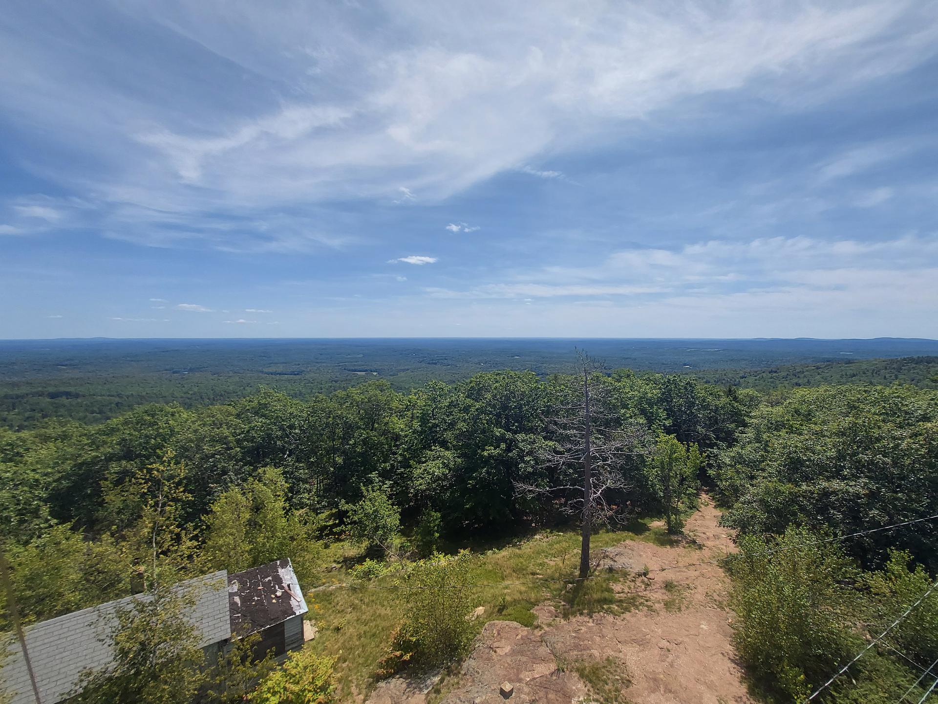 Overhead view of a small building and dirt path amidst a green forest.