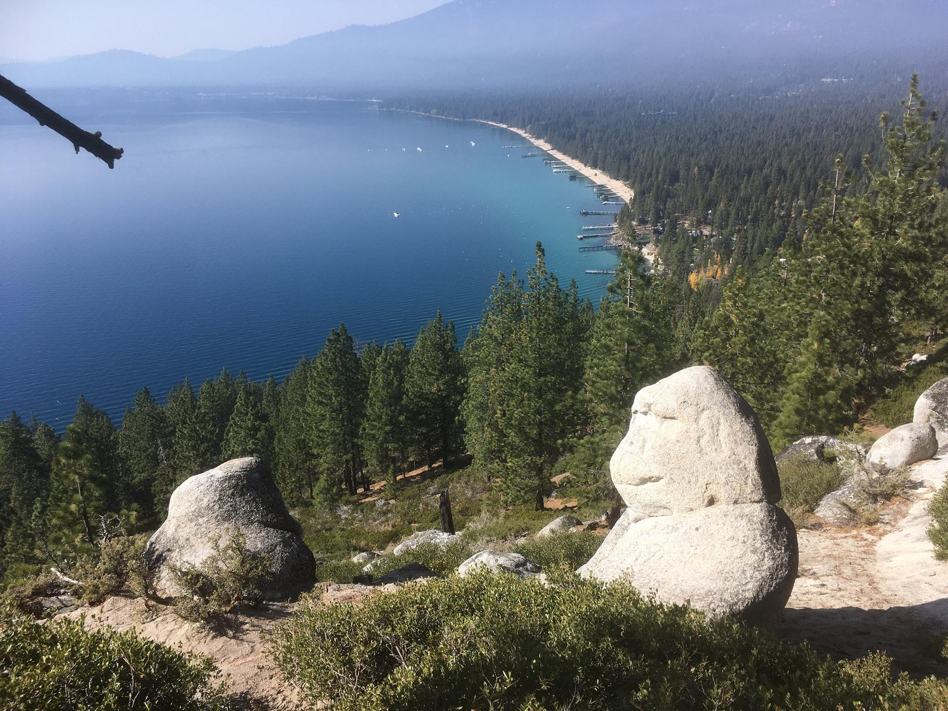 Two large rocks on a hill overlooking a vast blue lake and forested shoreline.