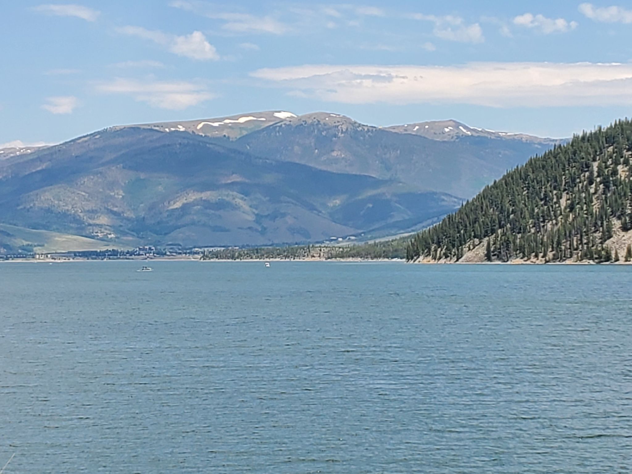 Blue lake, forested hills, distant snow-capped mountains, and small boats under cloudy sky. - Dillon Reservoir Recpath Loop