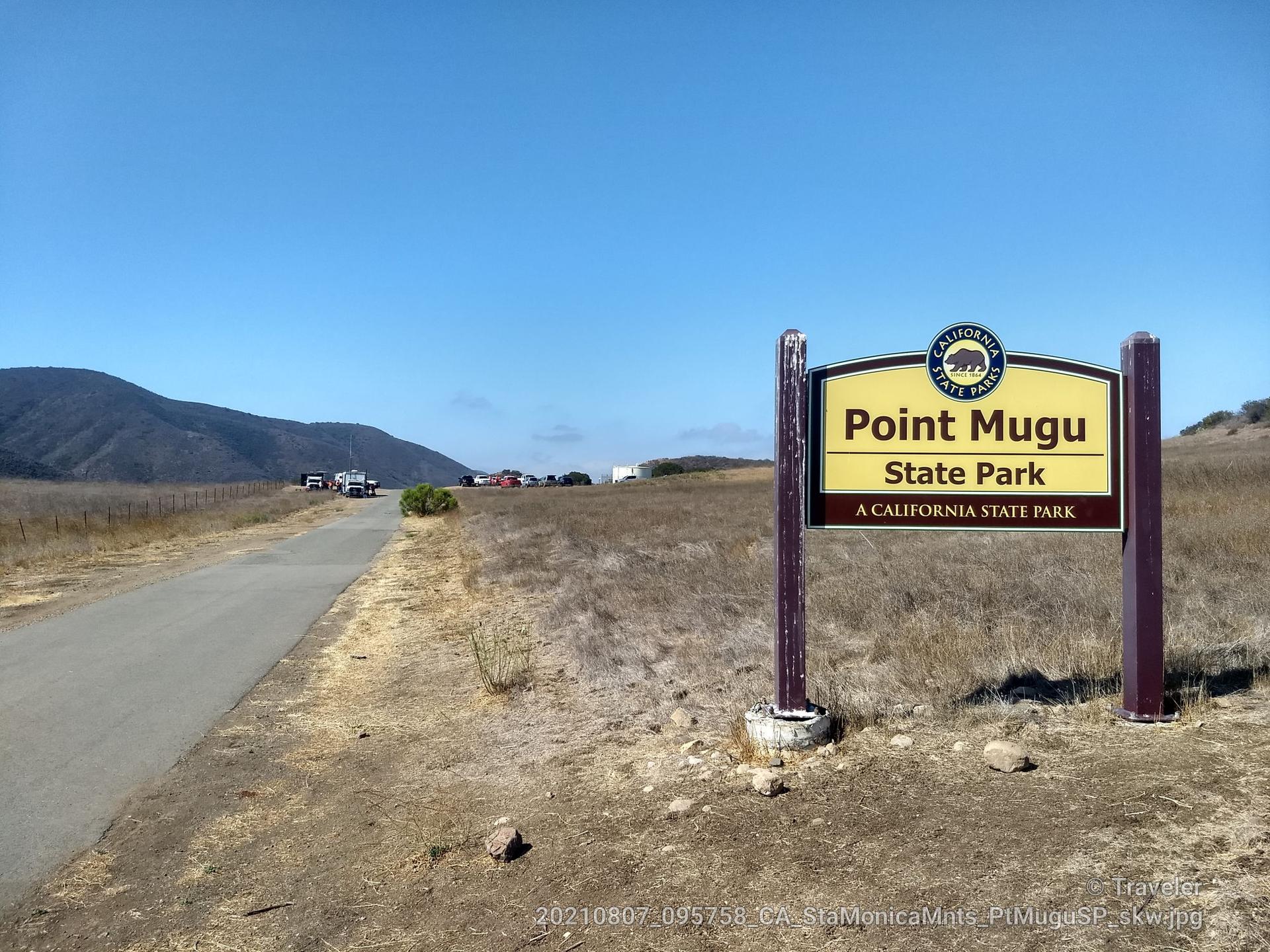 A wooden signpost next to a dirt road with distant mountains.