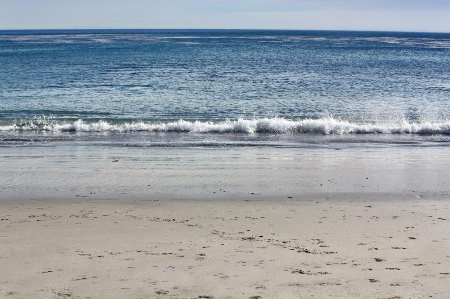 Ocean waves gently break on a wide, sandy beach under a clear sky.
