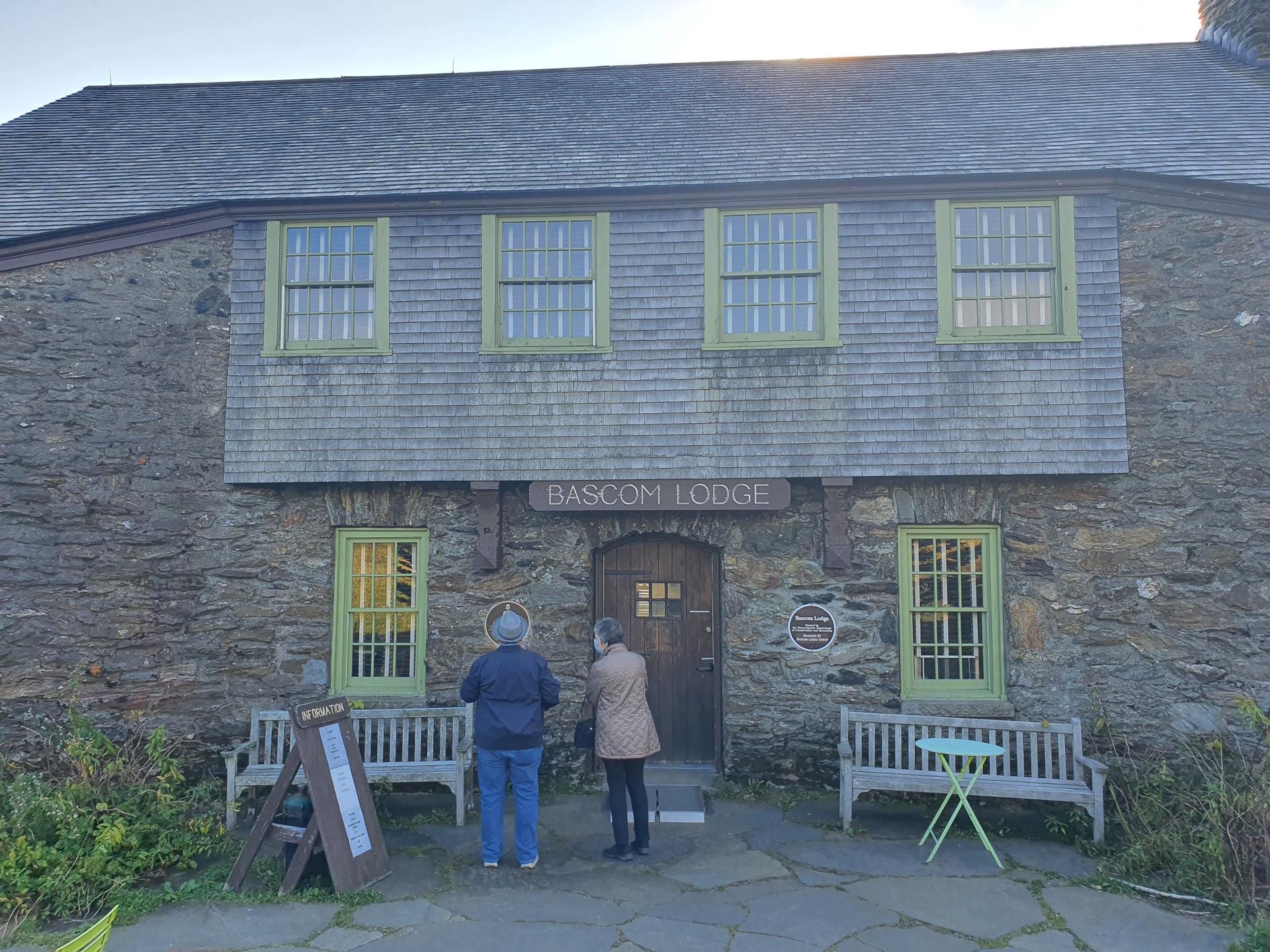 Two people stand outside a stone lodge with green-trimmed windows.