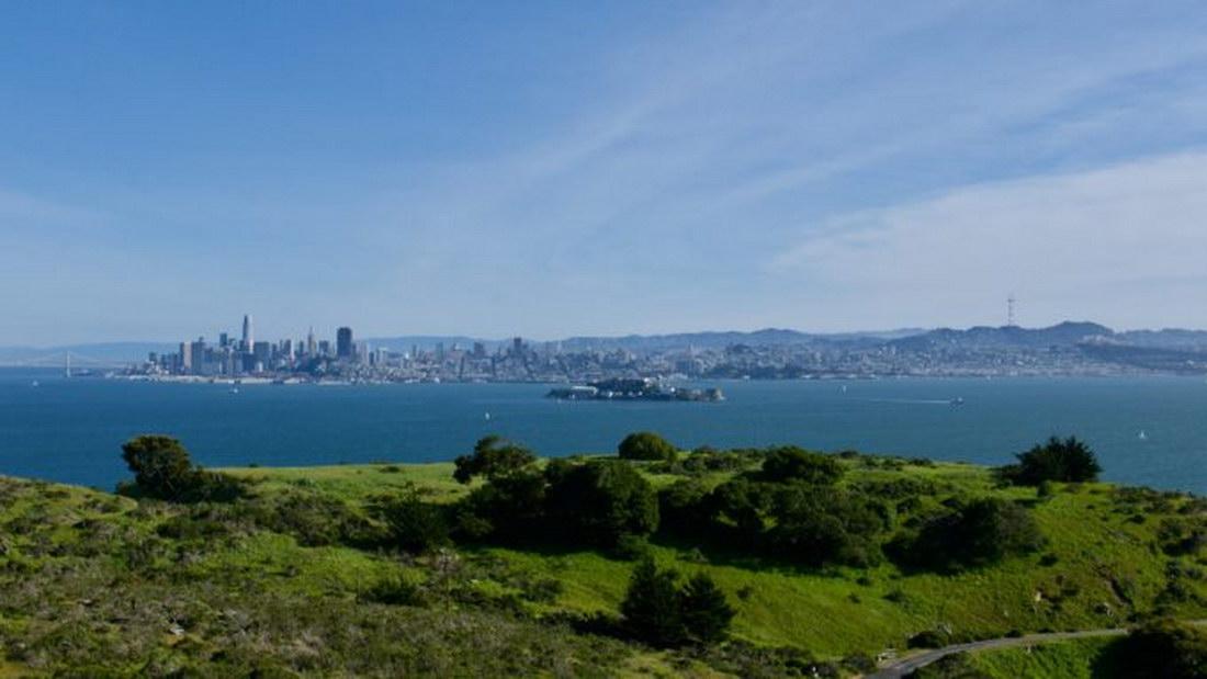 Distant city skyline across a wide bay, with green hills in the foreground.