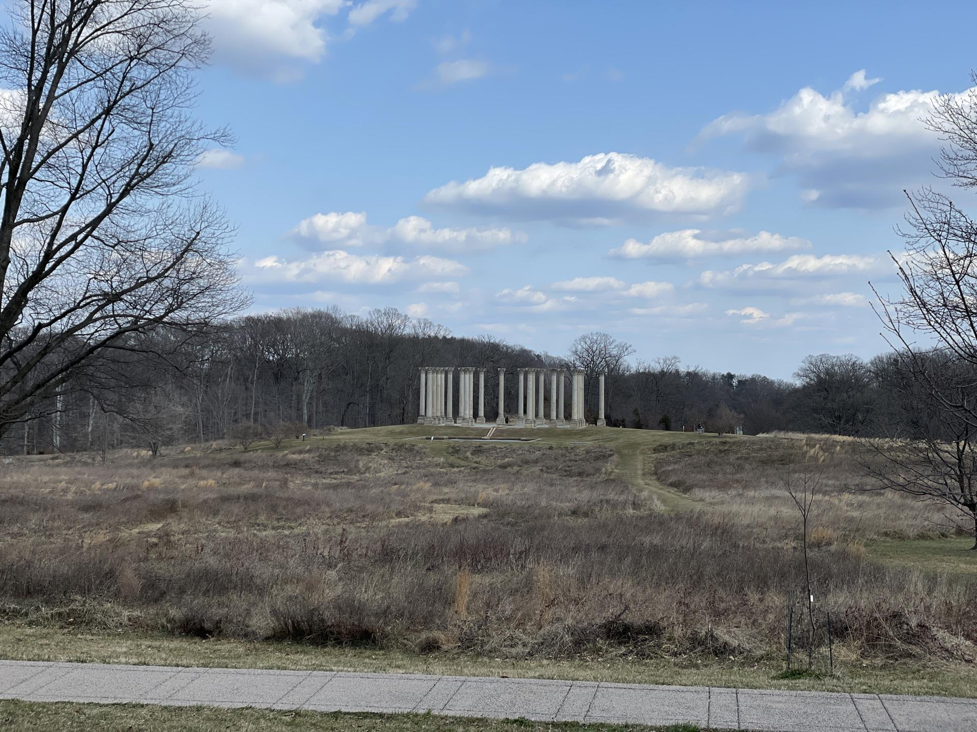 Distant stone columns stand on a hill in a dry, grassy landscape.