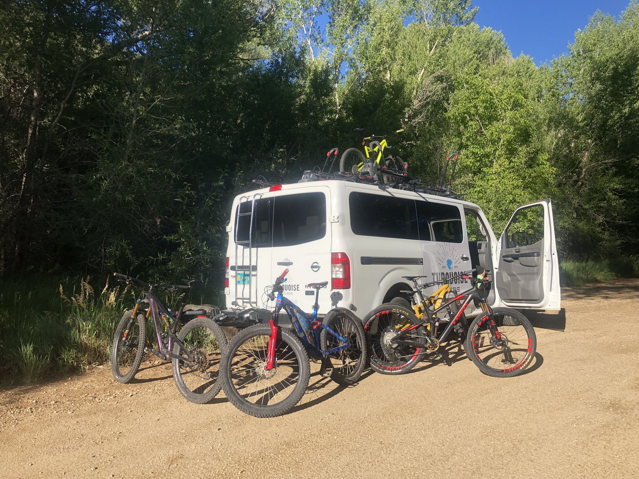 White van with bikes parked on a sunny dirt road near green trees. - South Boundary Trail to First Peak