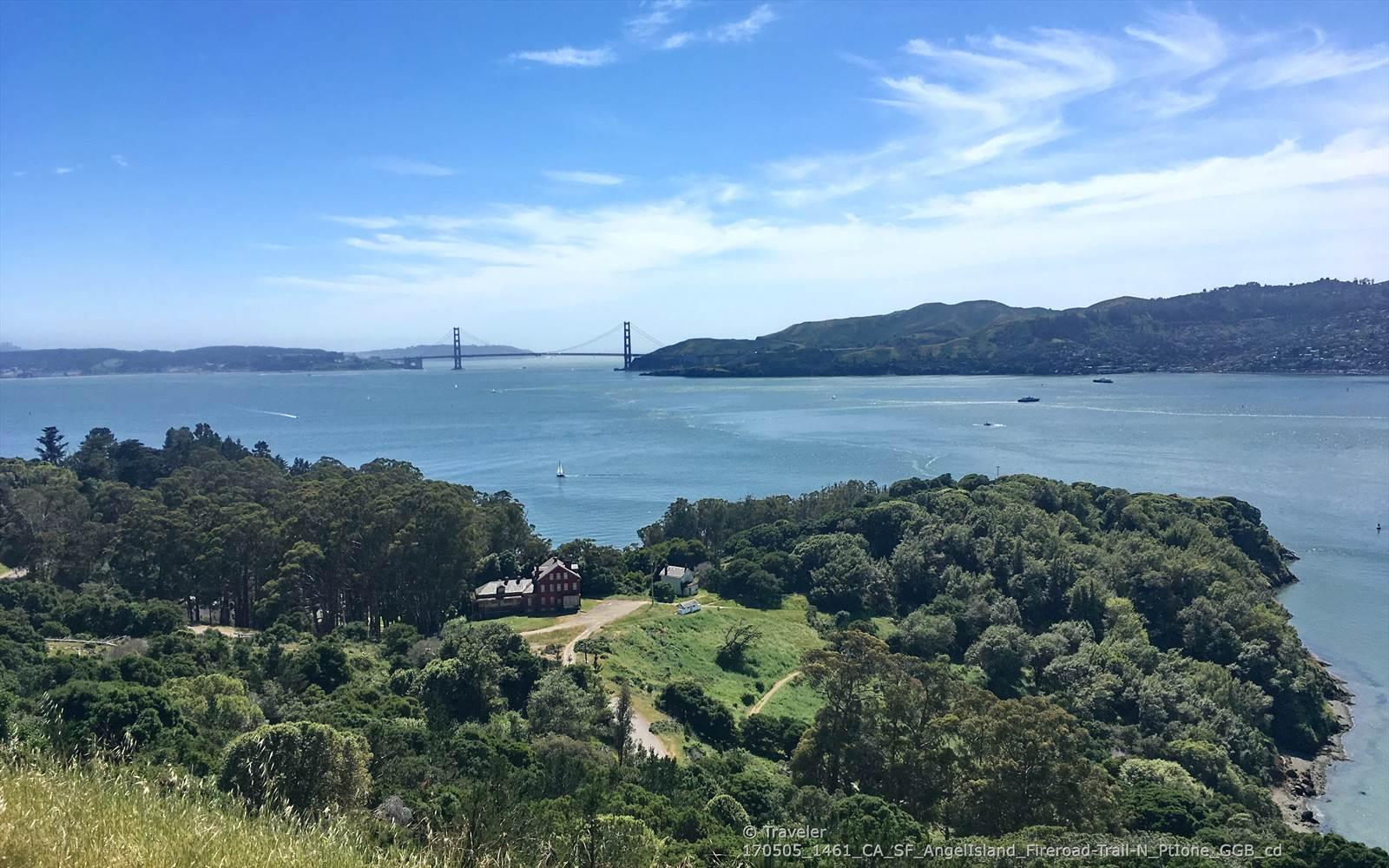 Distant bridge over a bay, with a red building on a green, tree-covered island.