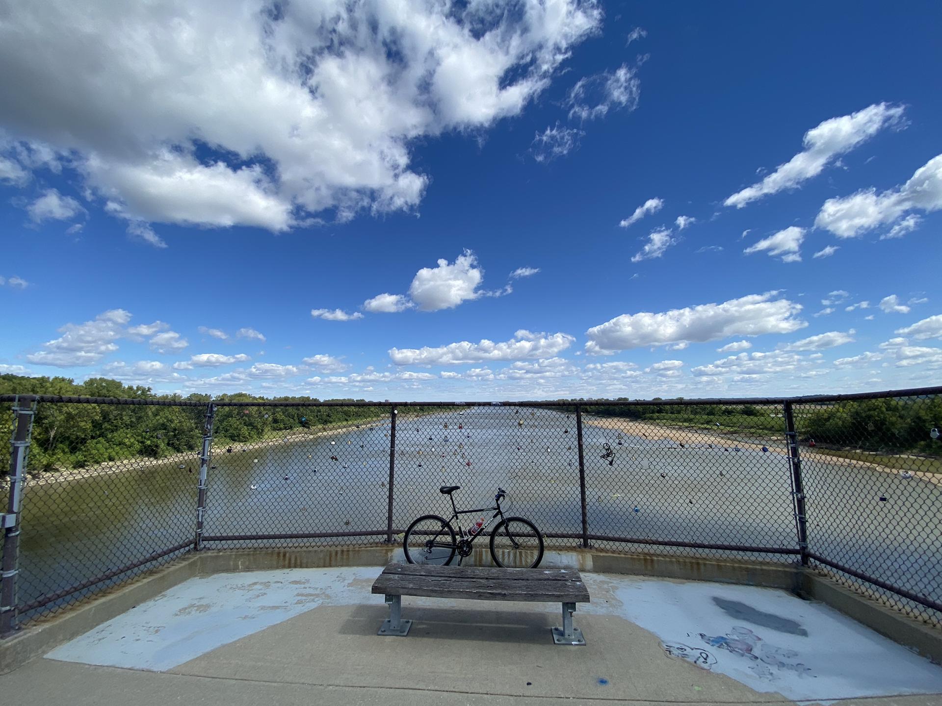 Bicycle parked on a bridge deck overlooking a river under a blue sky.