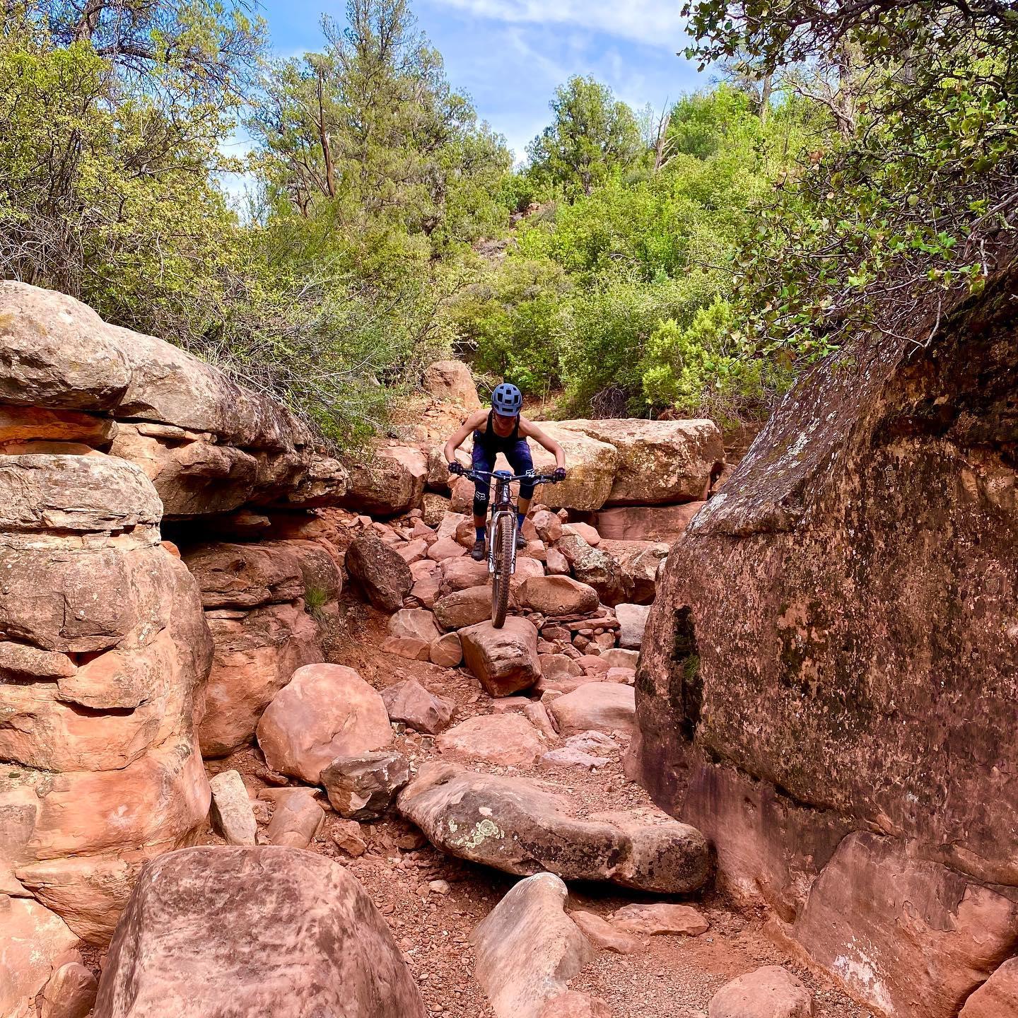 Person mountain biking through a challenging, rocky red canyon path.