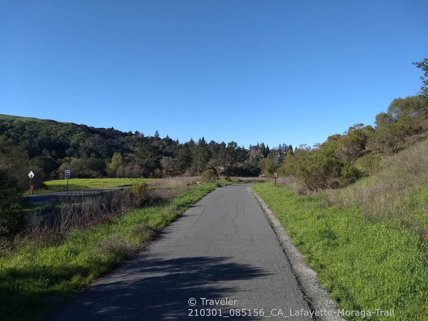 Paved path through grassy fields and hills under a clear blue sky.