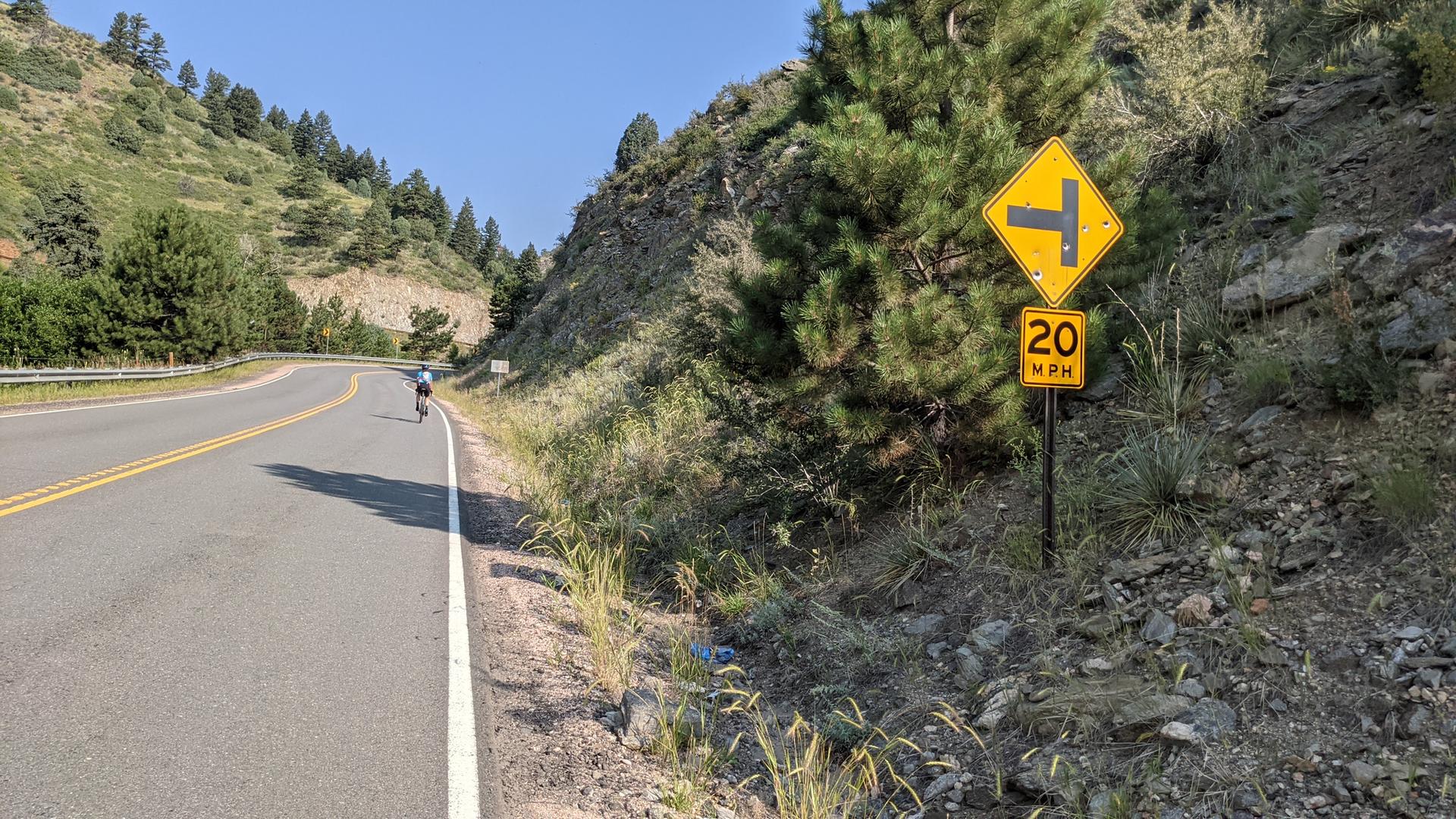 A person cycles on a winding mountain road under bright sunlight.