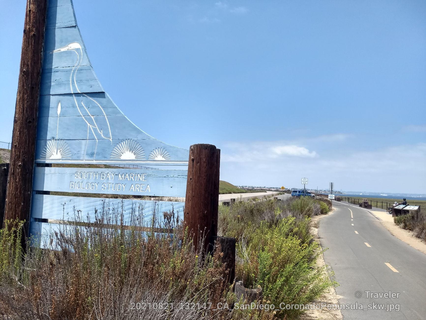 Blue sign with marine life illustration next to a road and dry shrubs.