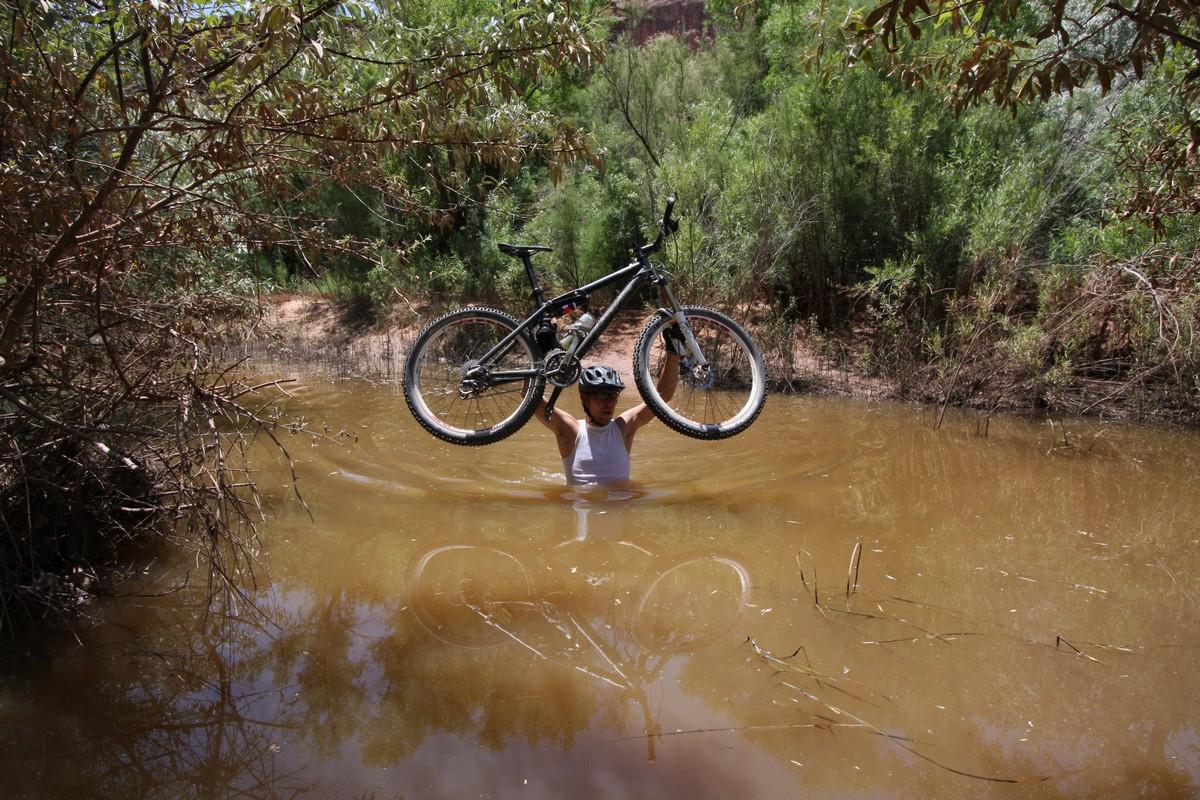 Person holding a mountain bike above their head in muddy water.