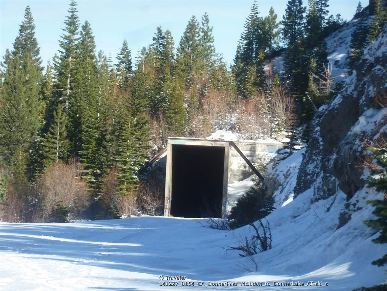 Dark tunnel entrance in a snowy forest next to a rock face.