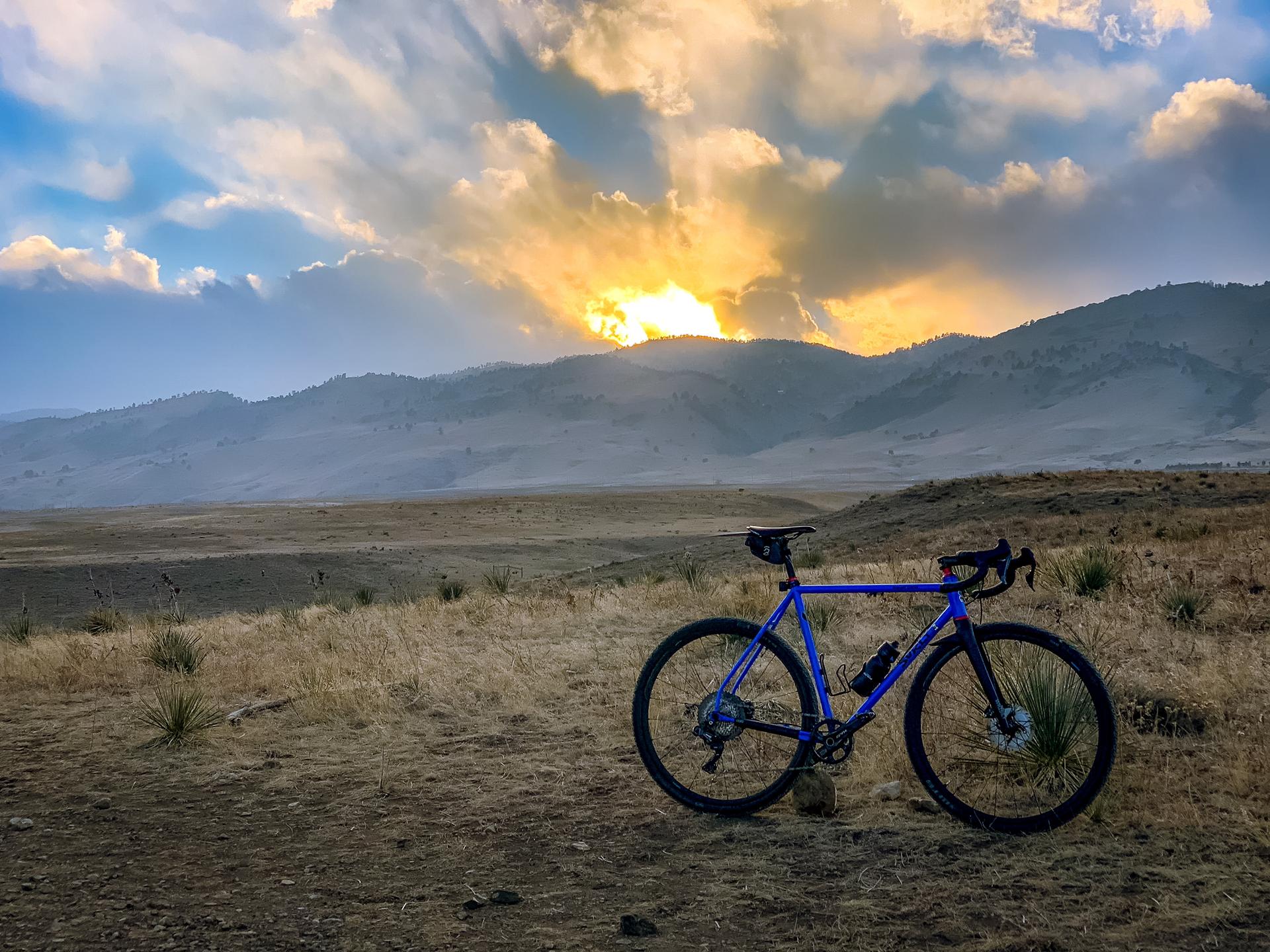 Blue bicycle on a dirt path with rolling hills and a vibrant sunset.