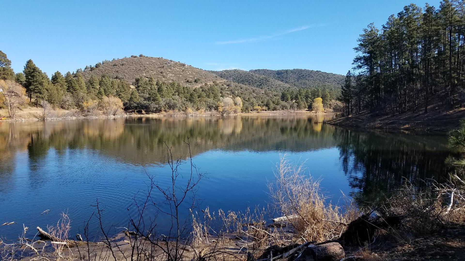 A calm lake reflects green hills and a clear blue sky.