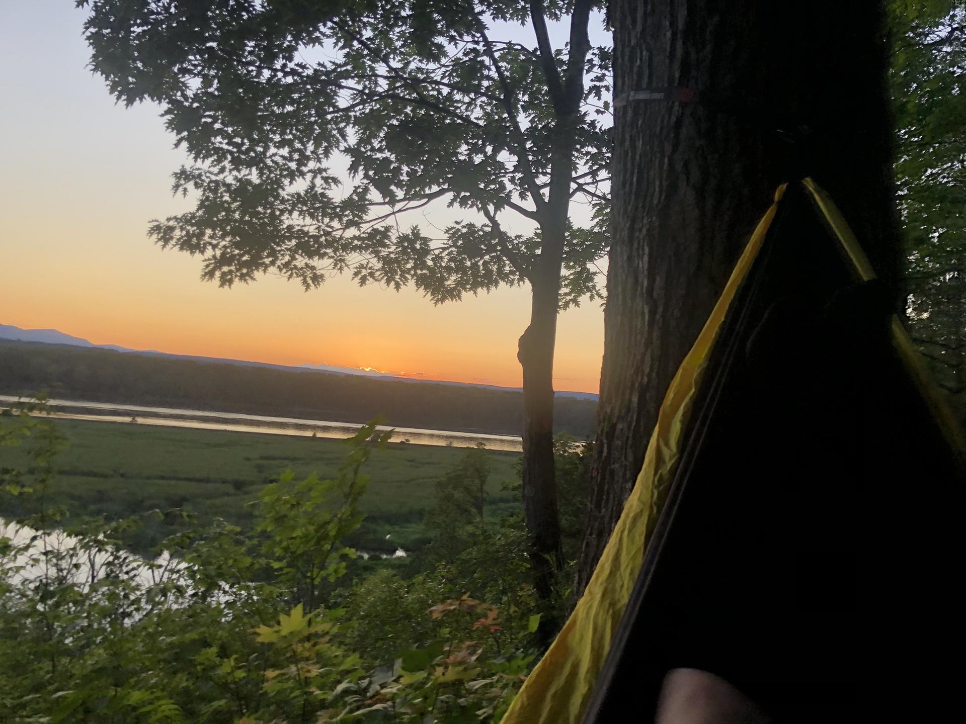 Hammock view of a river valley at sunset, with a person relaxing.