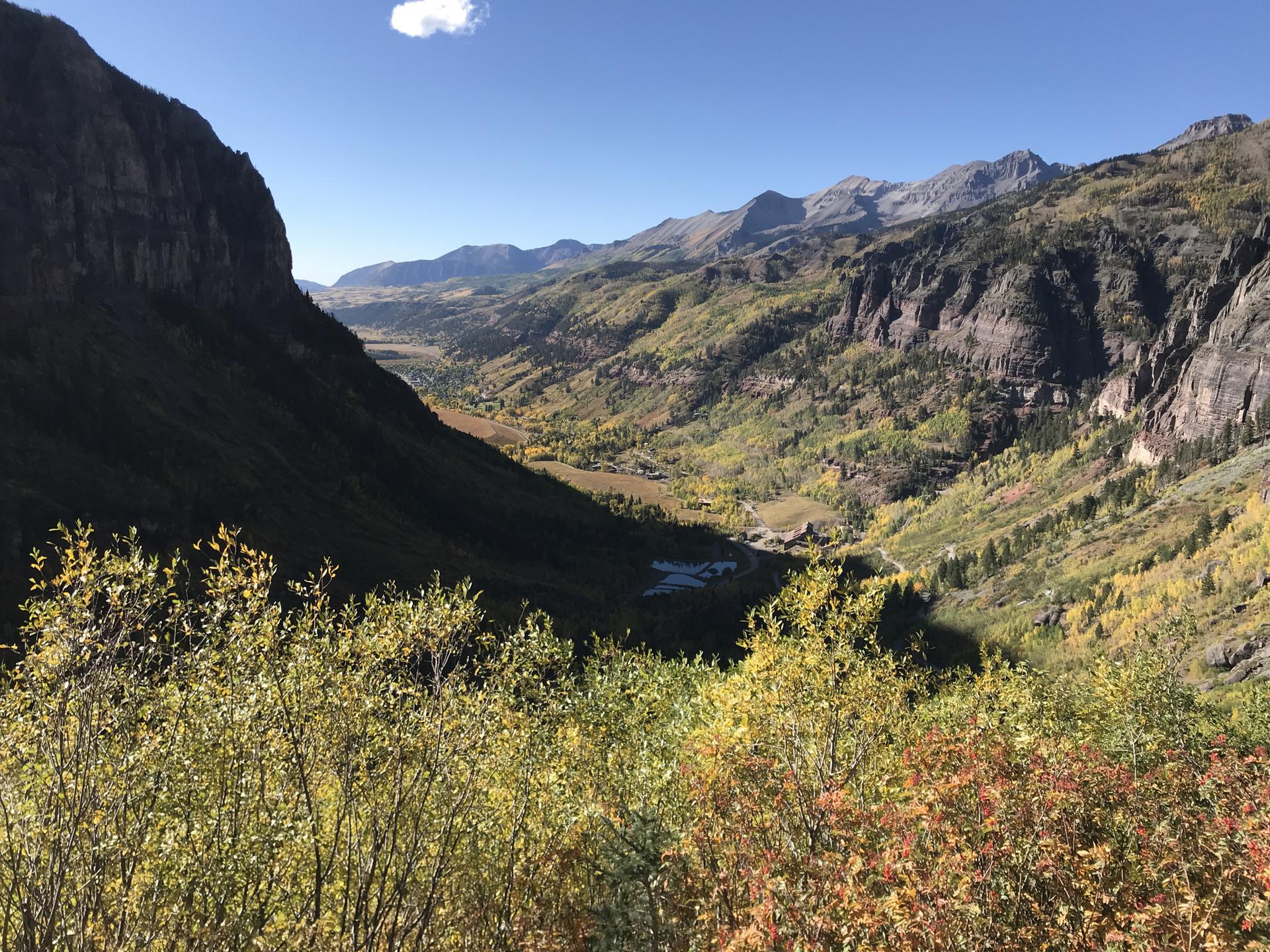 Expansive mountain valley with vibrant autumn trees under a clear blue sky.
