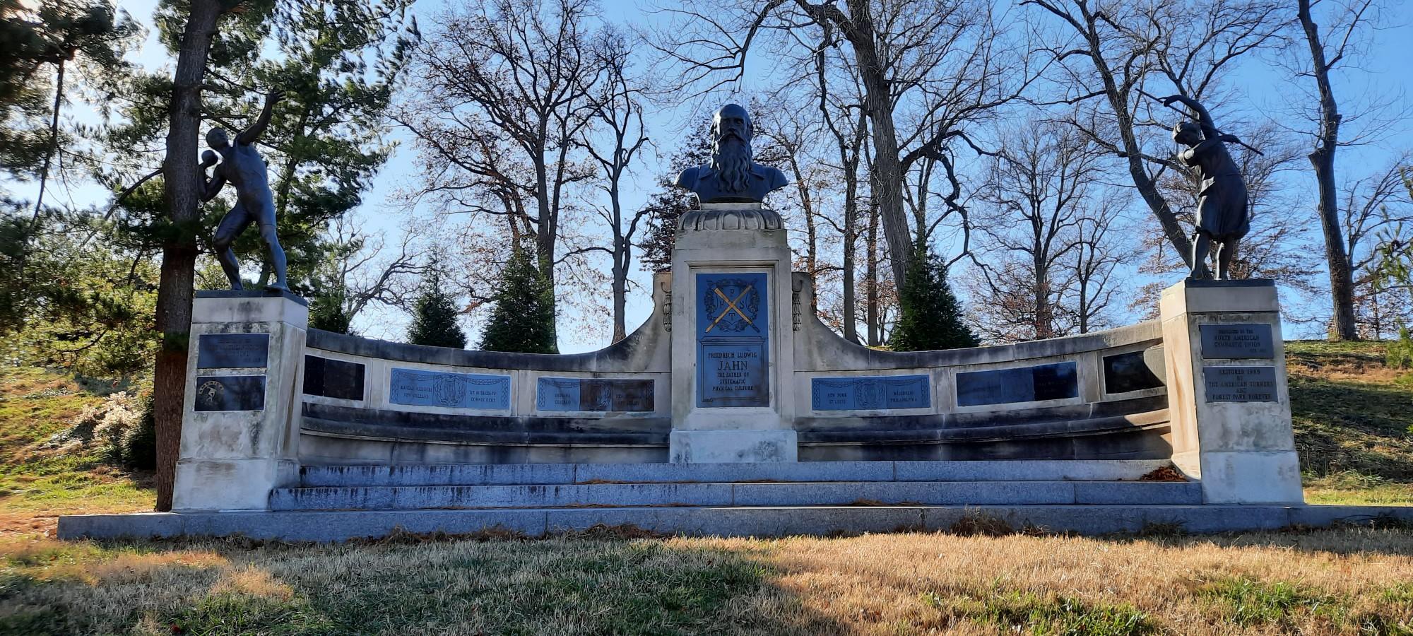 Large stone monument with statues and a bust under a clear sky.