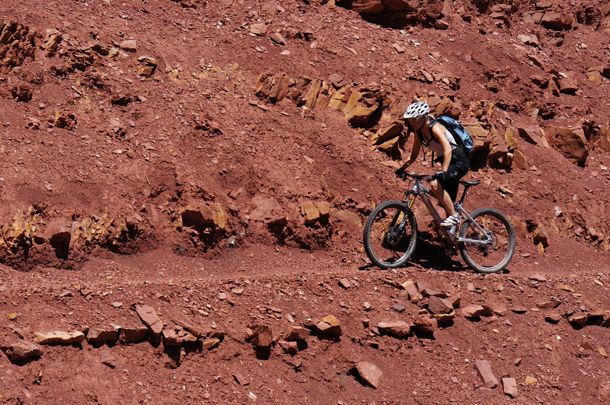 Person mountain biking on a red rocky trail under bright daylight. - Pipe Dream – Best of Moab MTB Trails