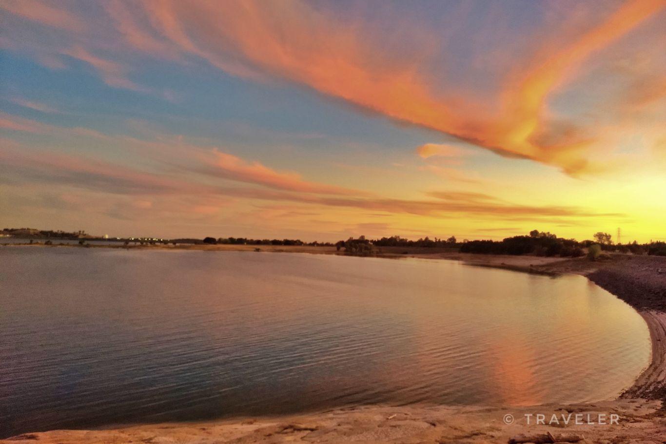 A wide lake reflects a vibrant sunset with orange and pink clouds.