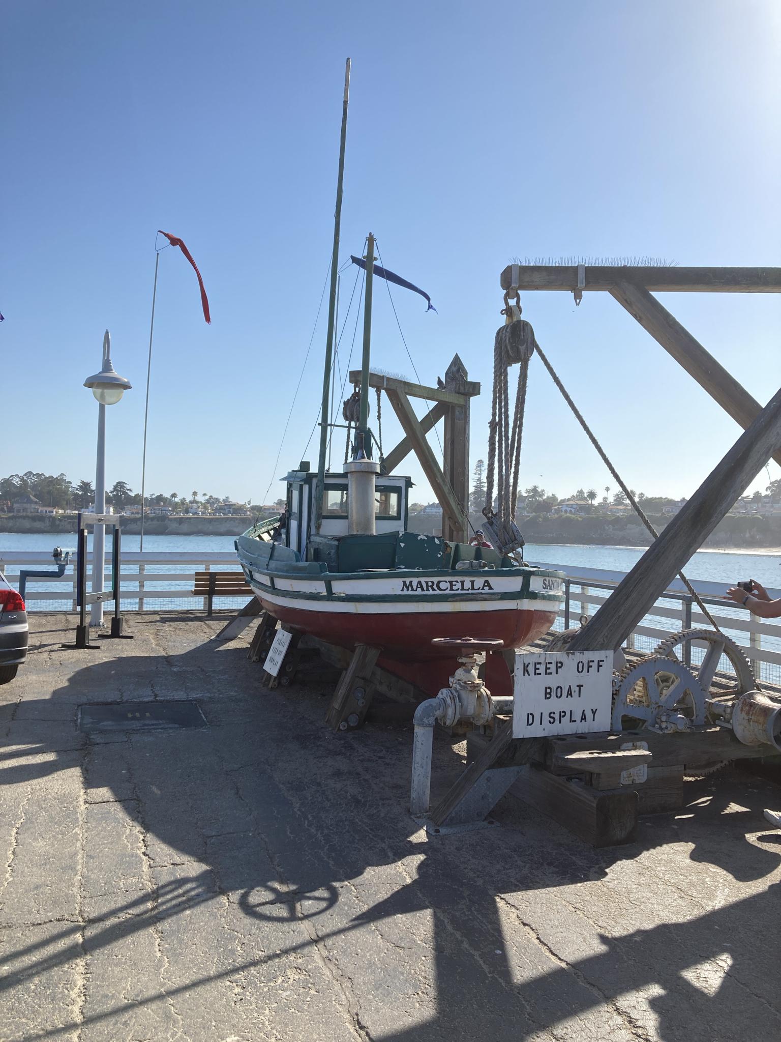 A red and green display boat on a sunny wooden pier.