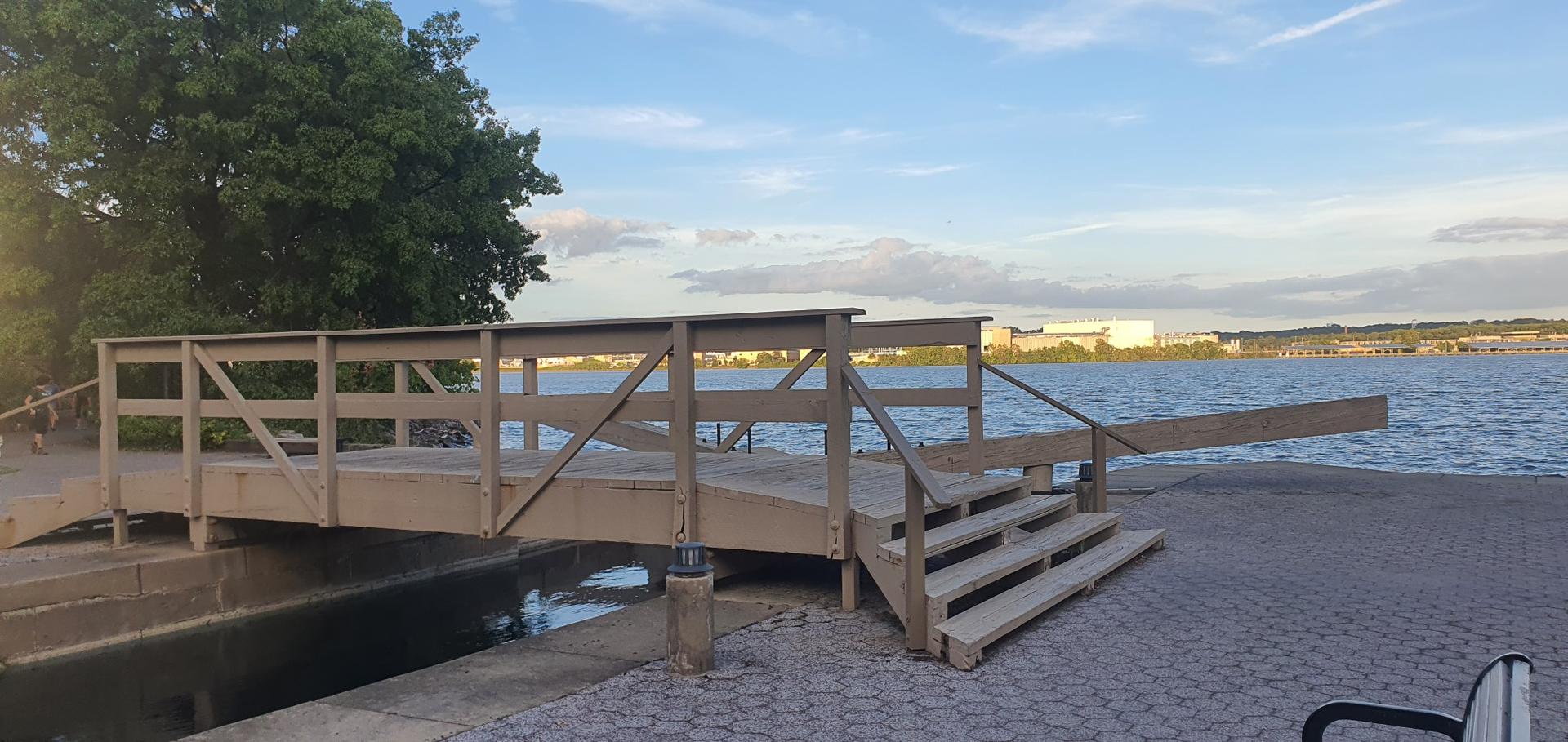 Wooden bridge and steps leading to a wide river under a bright sky.