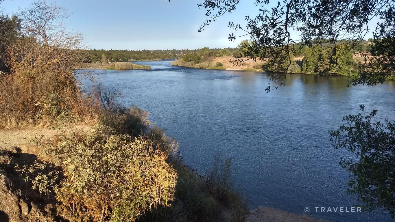 Wide river flowing through a natural landscape under bright sunlight.