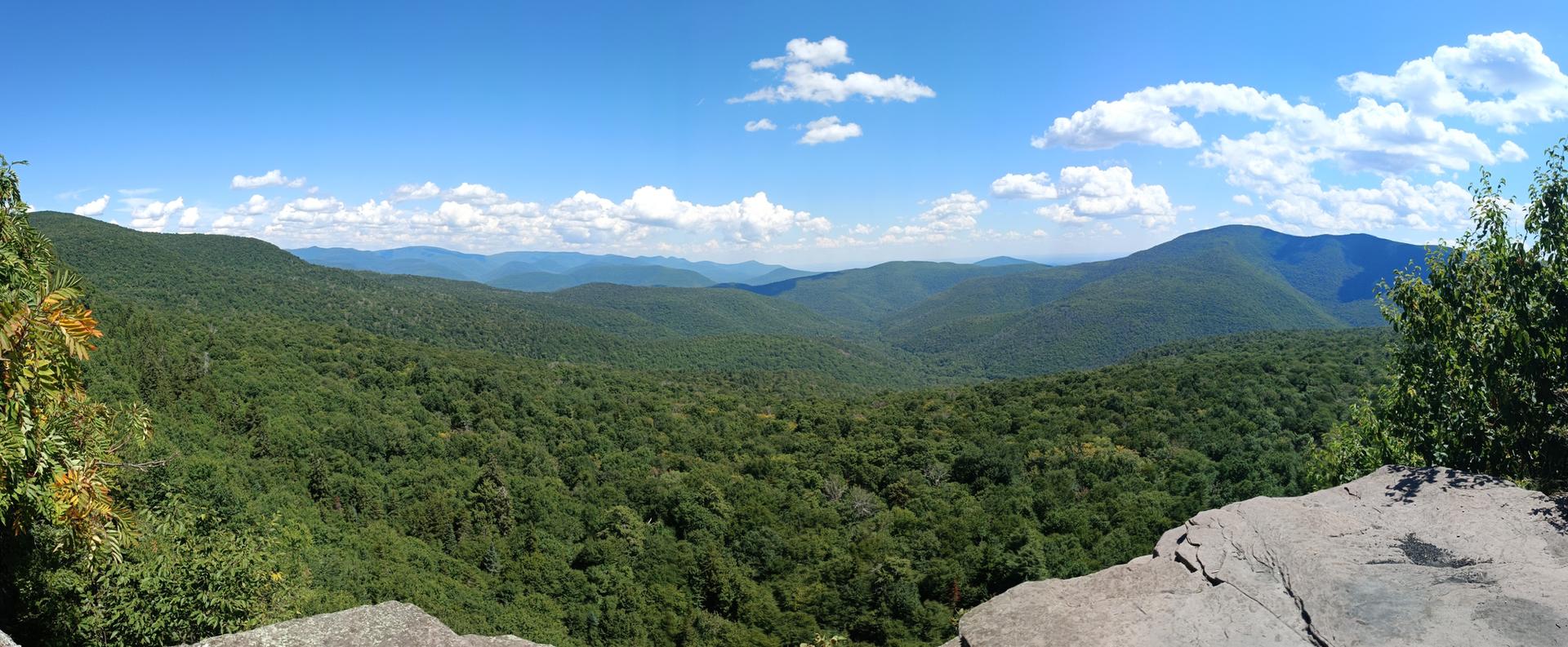 Panoramic view of lush green mountains under a bright blue sky with clouds.