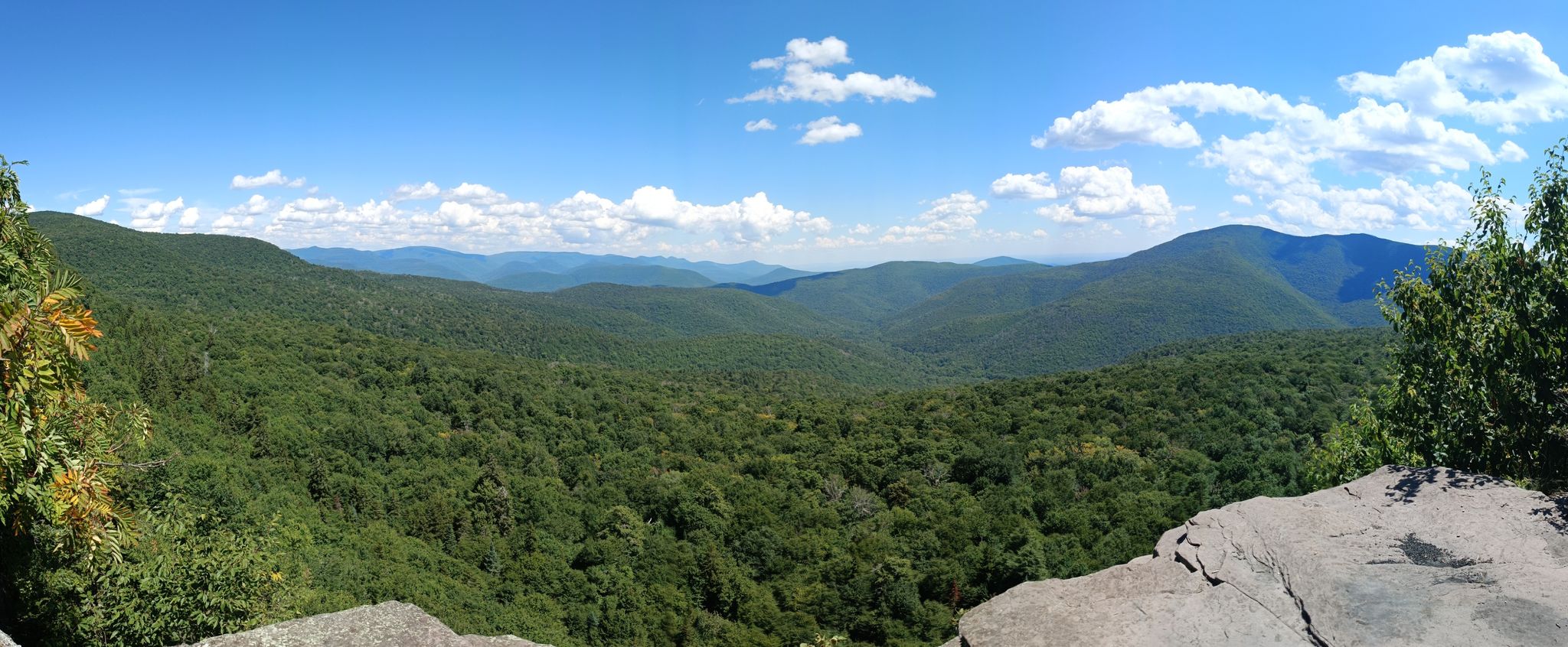 Panoramic view of lush green mountains under a bright blue sky with clouds. - Giant Ledge Trail