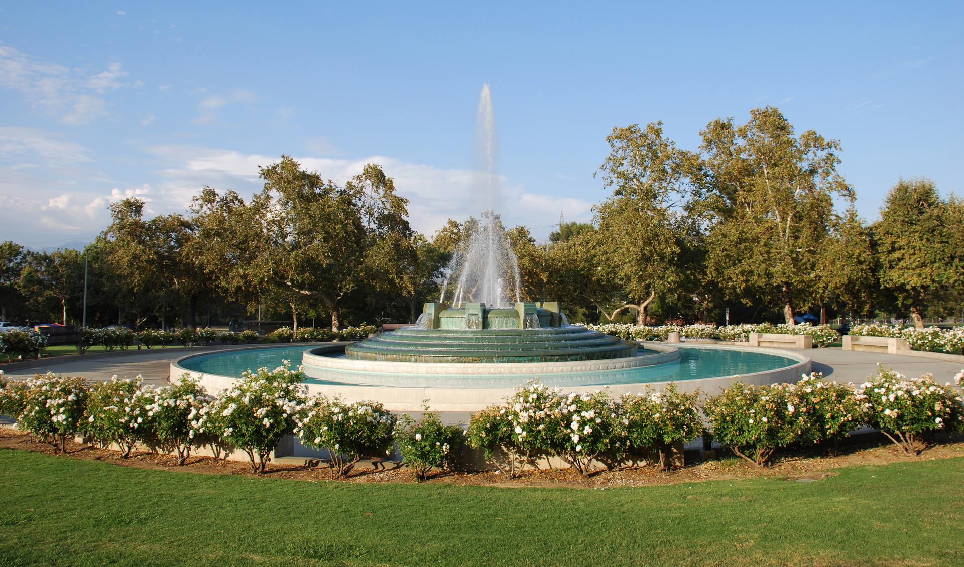 A large tiered fountain surrounded by green grass and trees on a bright day.