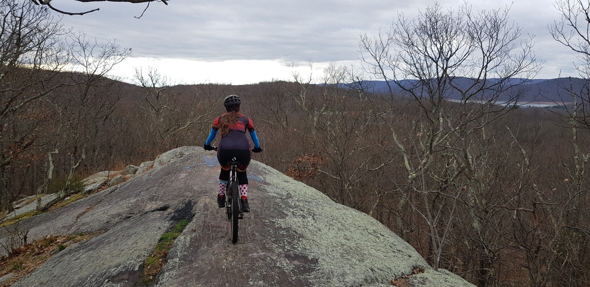 Mountain biker on a rocky ridge overlooking a vast, cloudy landscape. - Ringwood Crossover and Mountain Bike Loop