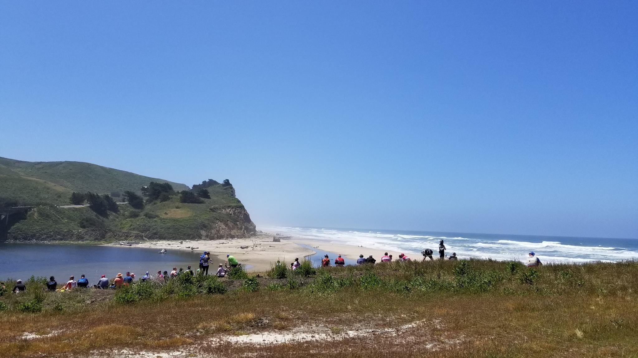 Many people gathered on a sunny beach next to cliffs and ocean.
