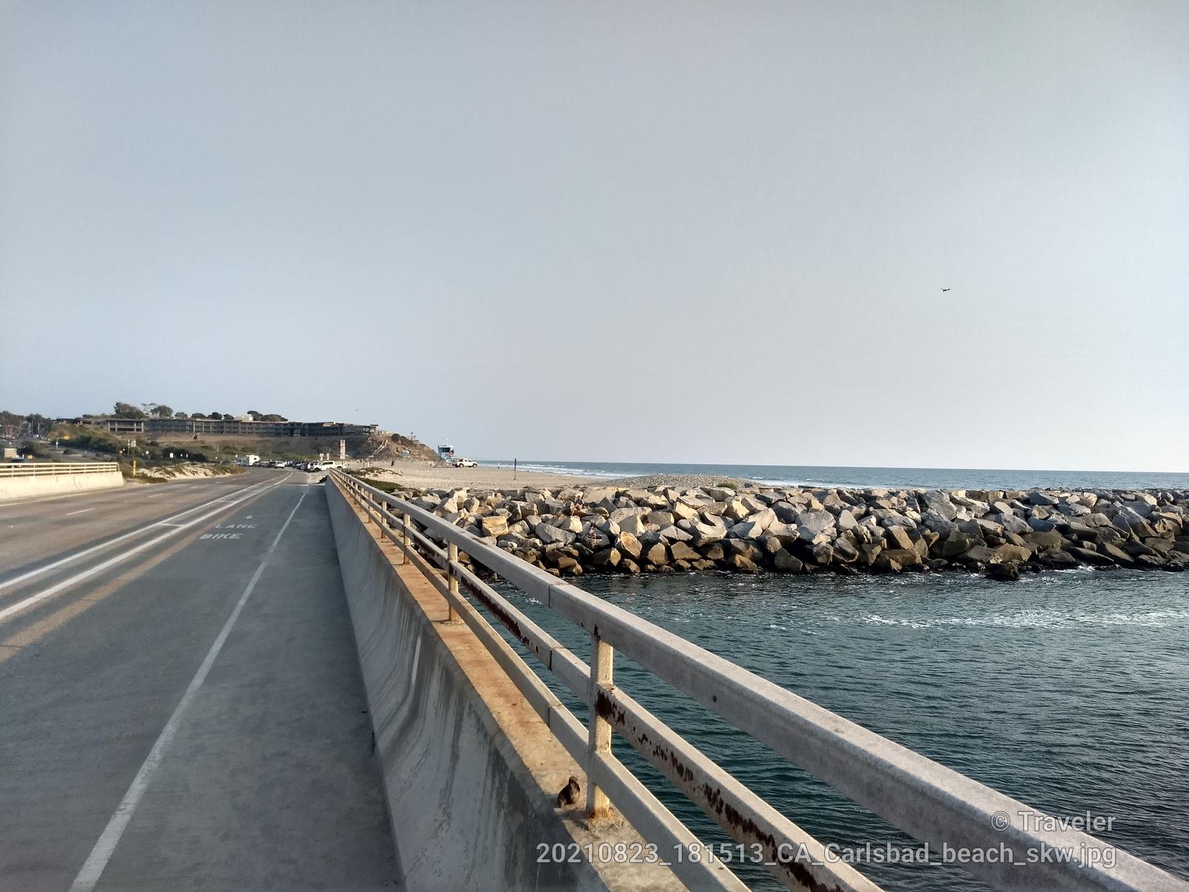 Bridge over water next to a rocky jetty, leading to a distant beach.