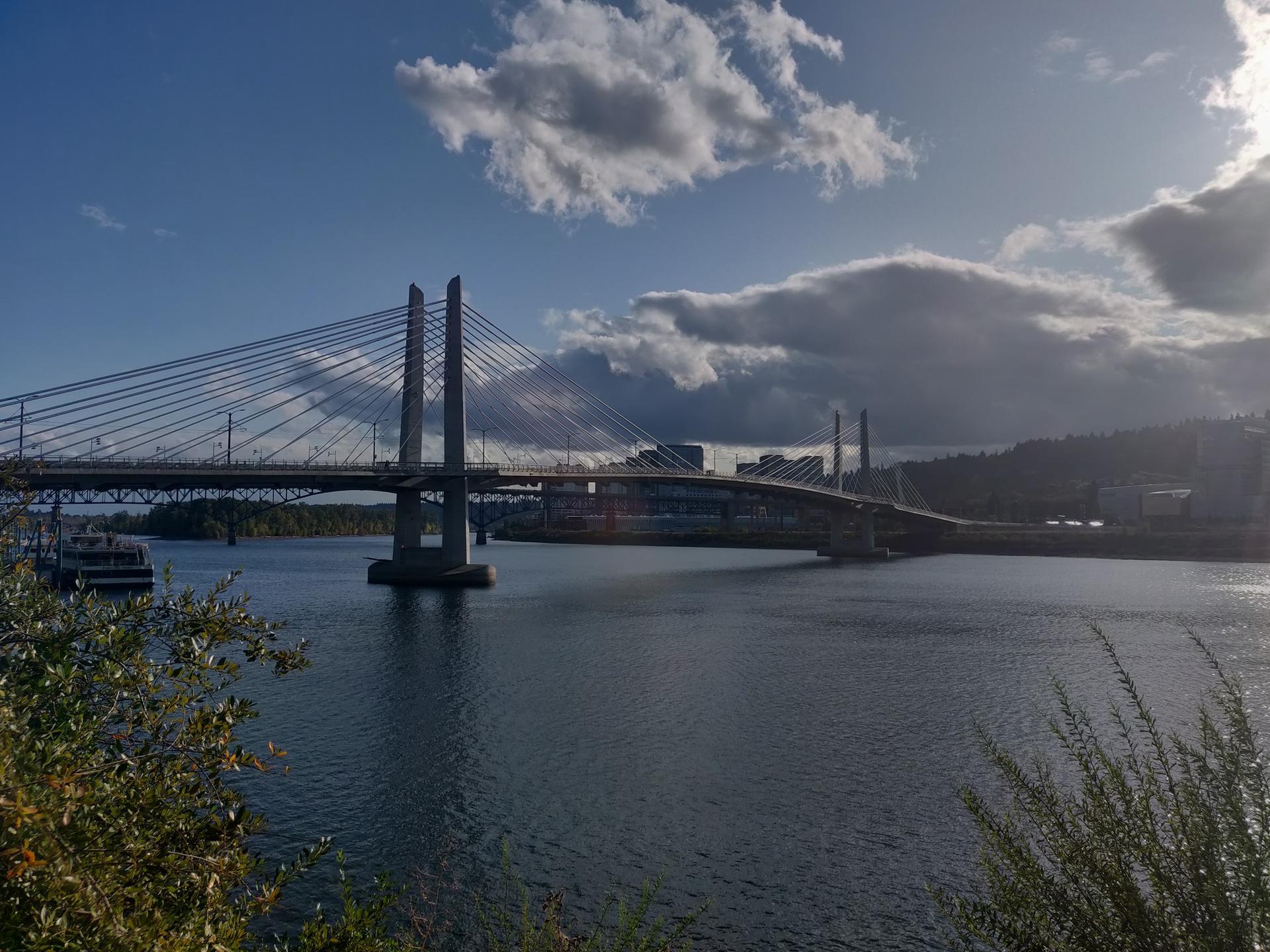 Modern cable-stayed bridge over a river under a partly cloudy sky.