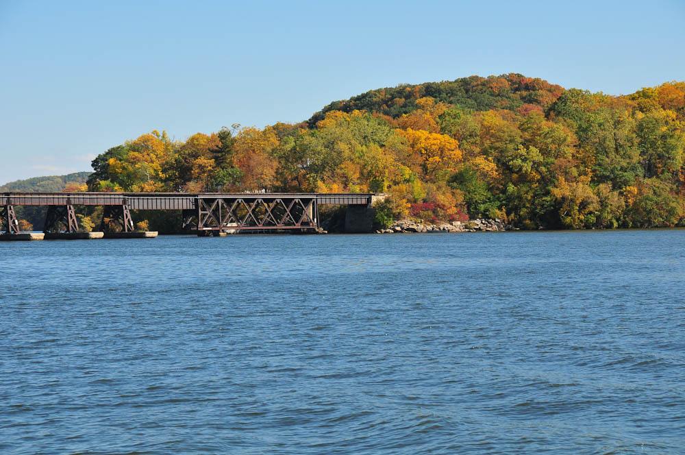 A long bridge spans wide water, backed by hills with vibrant autumn trees.