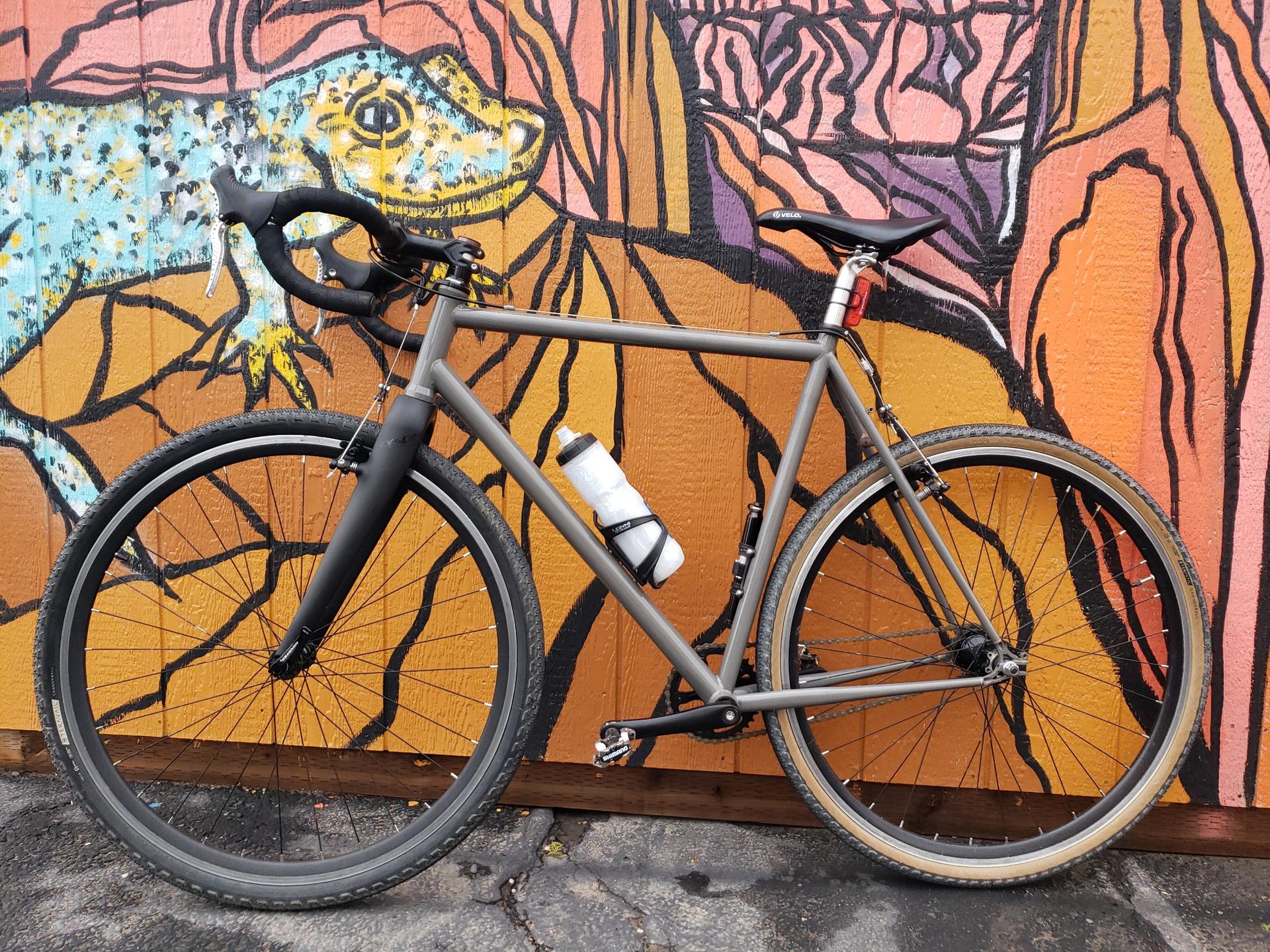 A gray bicycle with a water bottle leans against a vibrant, painted wall.