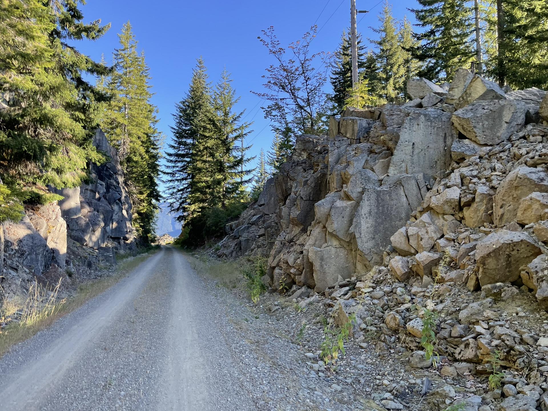 A gravel road cuts through a rocky, forested landscape under a clear sky.