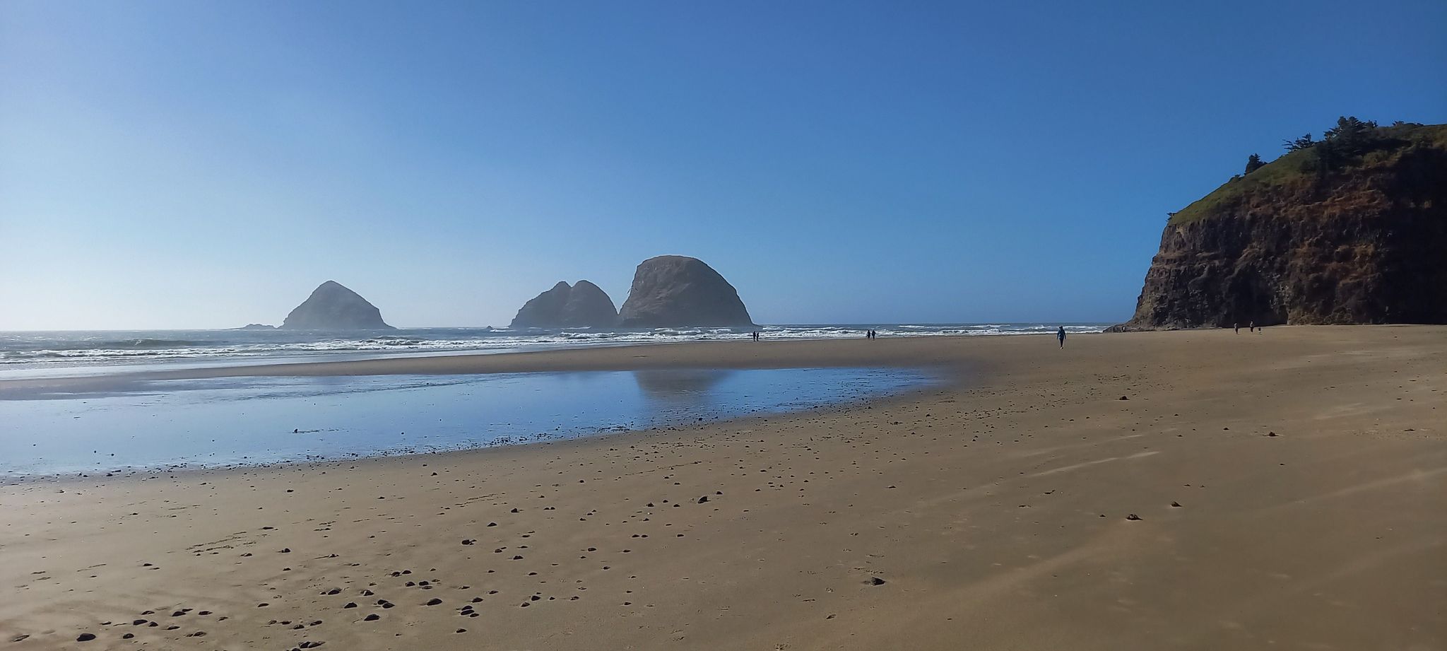 Expansive sandy beach with sea stacks, ocean, and distant people under clear sky. - Oceanside Beach to Tunnel Beach Trail