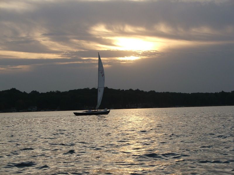 Sailboat silhouetted on water at sunset with cloudy sky and distant trees. - Spring Valley Park – Gull Lake loop from Gull Lake
