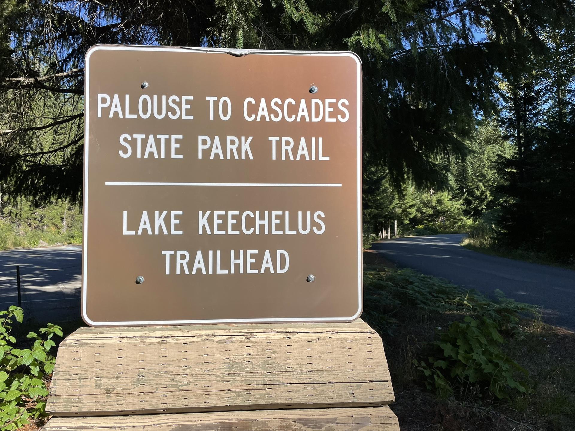 Brown trail sign on a wooden post, surrounded by green foliage and trees.