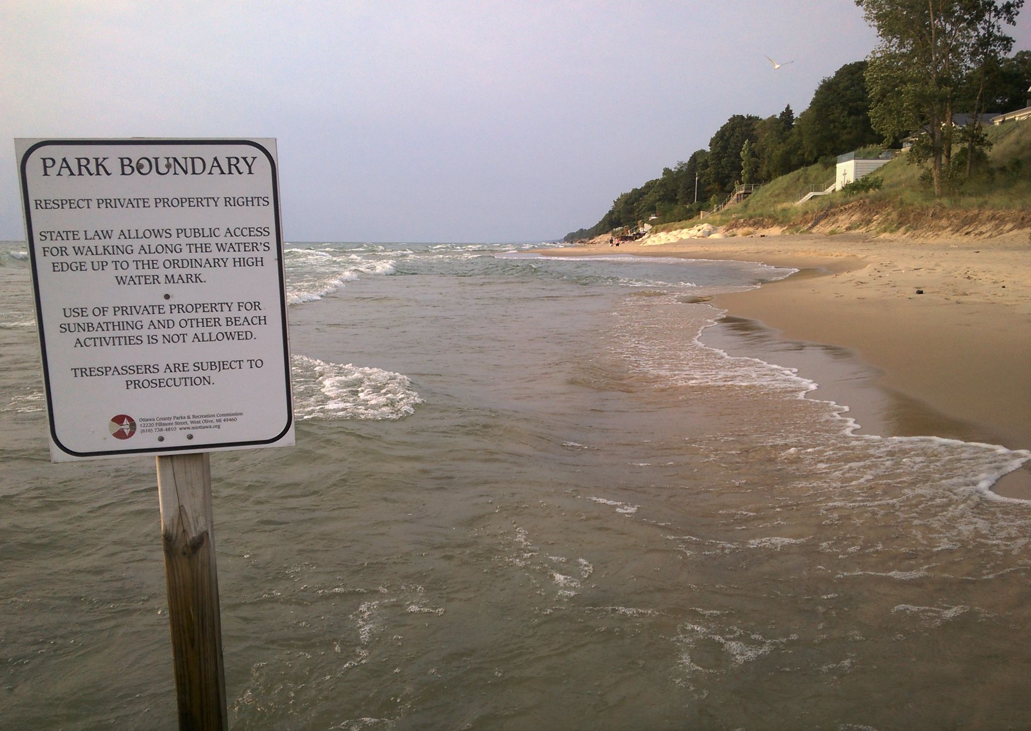 Beach boundary sign in shallow water next to sandy shore and waves. - Holland State Park – Ottawa Beach loop from Holland