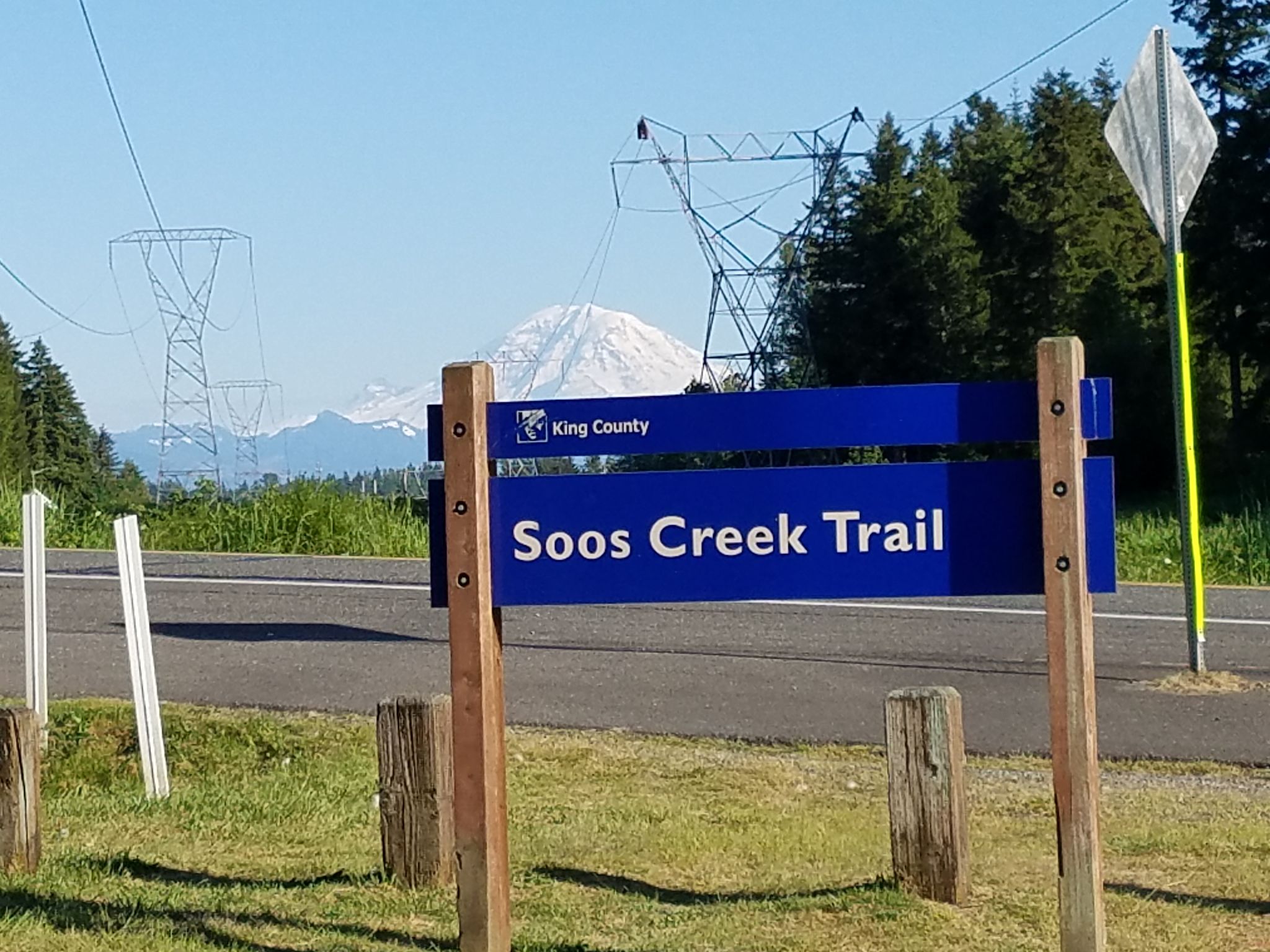 A blue sign by a road with power lines and a snowy mountain. - Soos Creek Trail