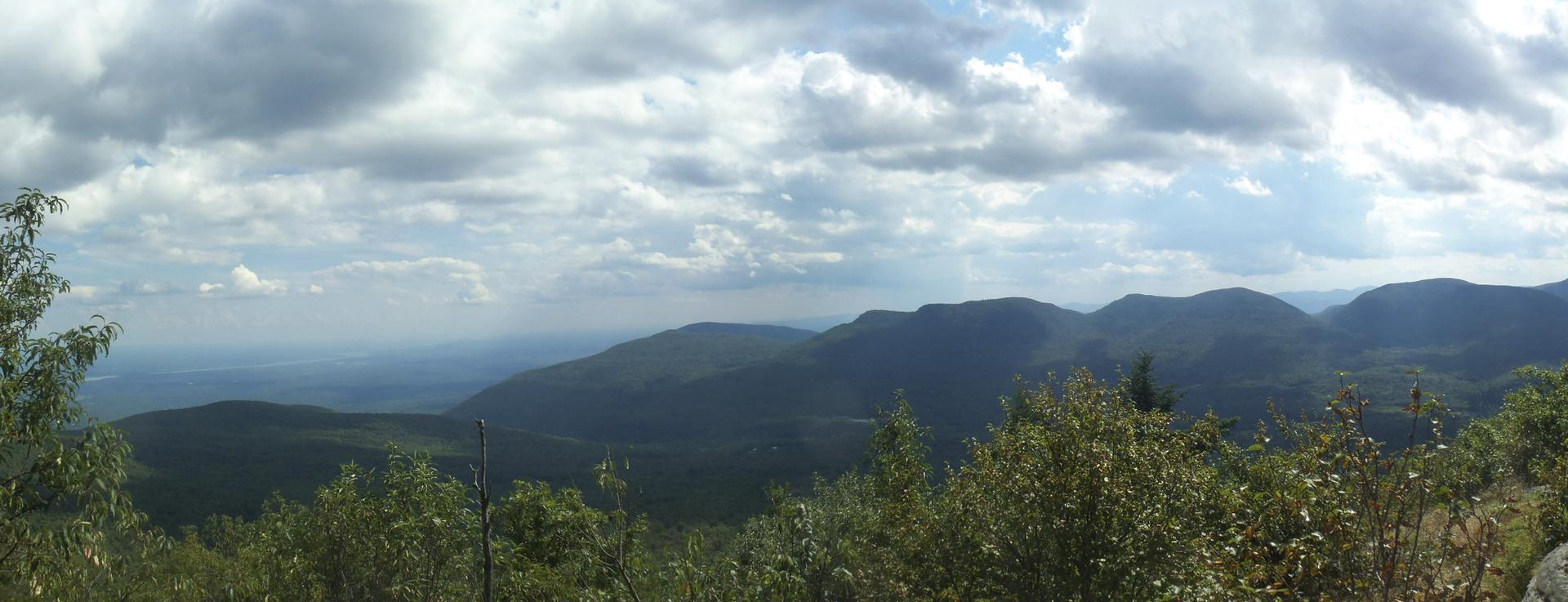 Panoramic view of dark green mountains and a hazy valley under a cloudy sky.