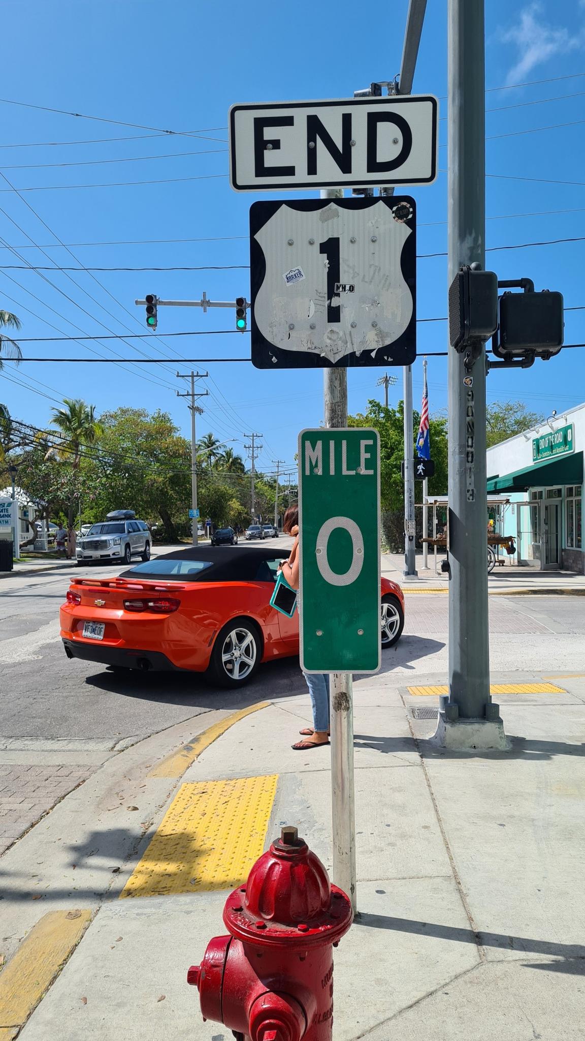 Street signs, a red fire hydrant, and a red car on a sunny urban street.