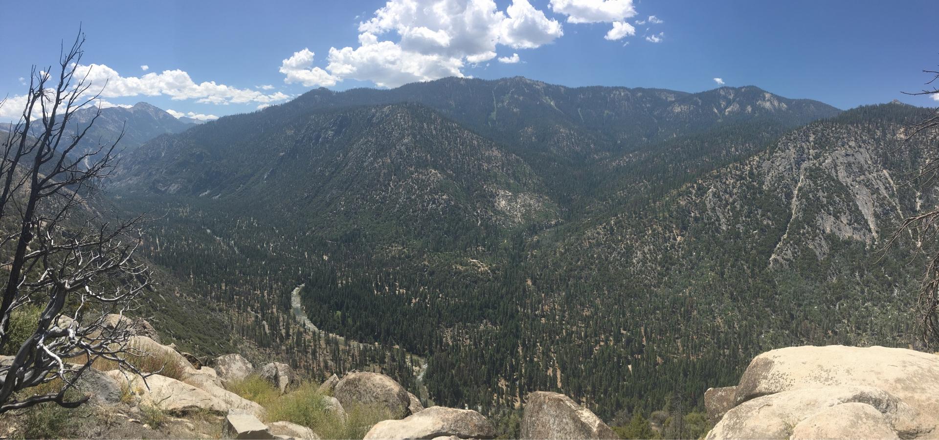 Panoramic view of vast forested mountains under a partly cloudy sky.