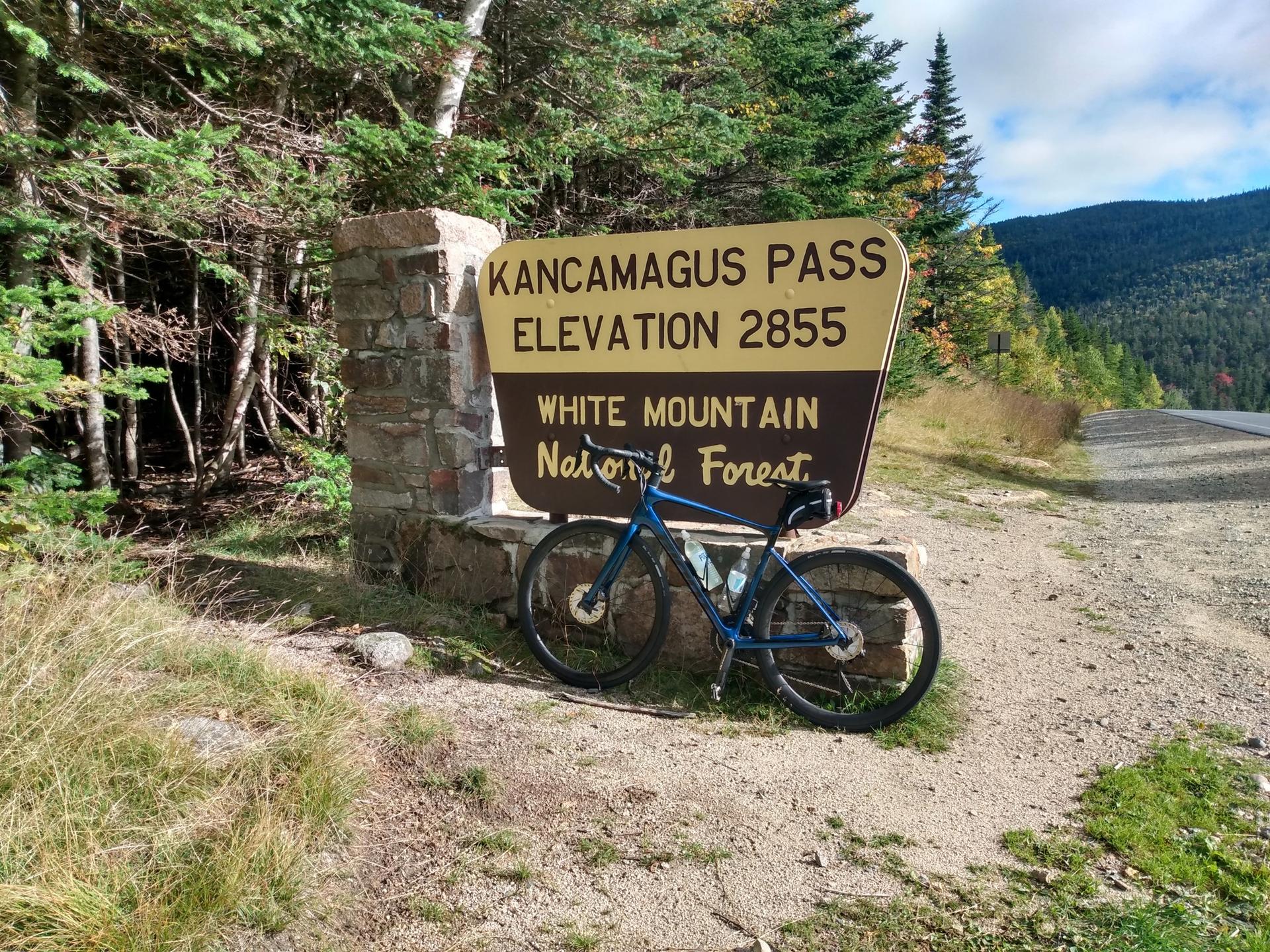 Blue bicycle leaning against a large sign on a dirt path.