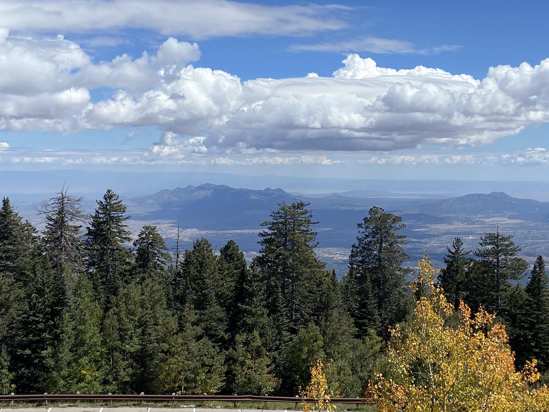 Expansive mountain vista with green and yellow trees under blue sky.